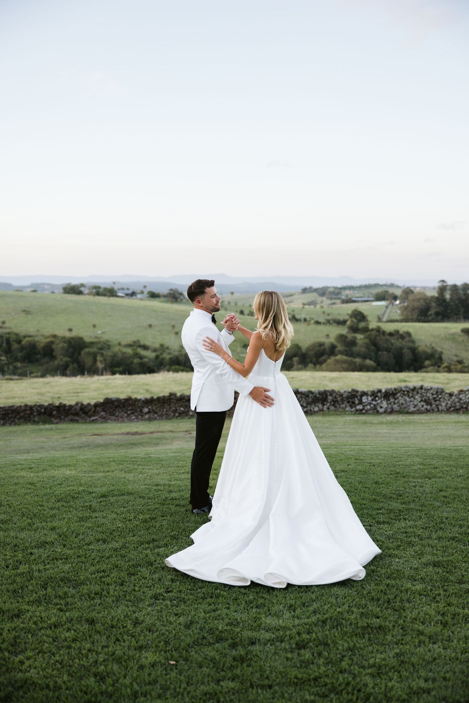 A bride and groom share an intimate dance moment on a grassy hillside.