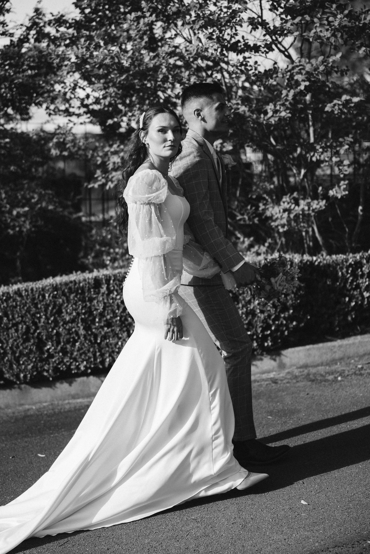 Black and white photo of a bride in a flowing gown embracing a groom in a suit outdoors.