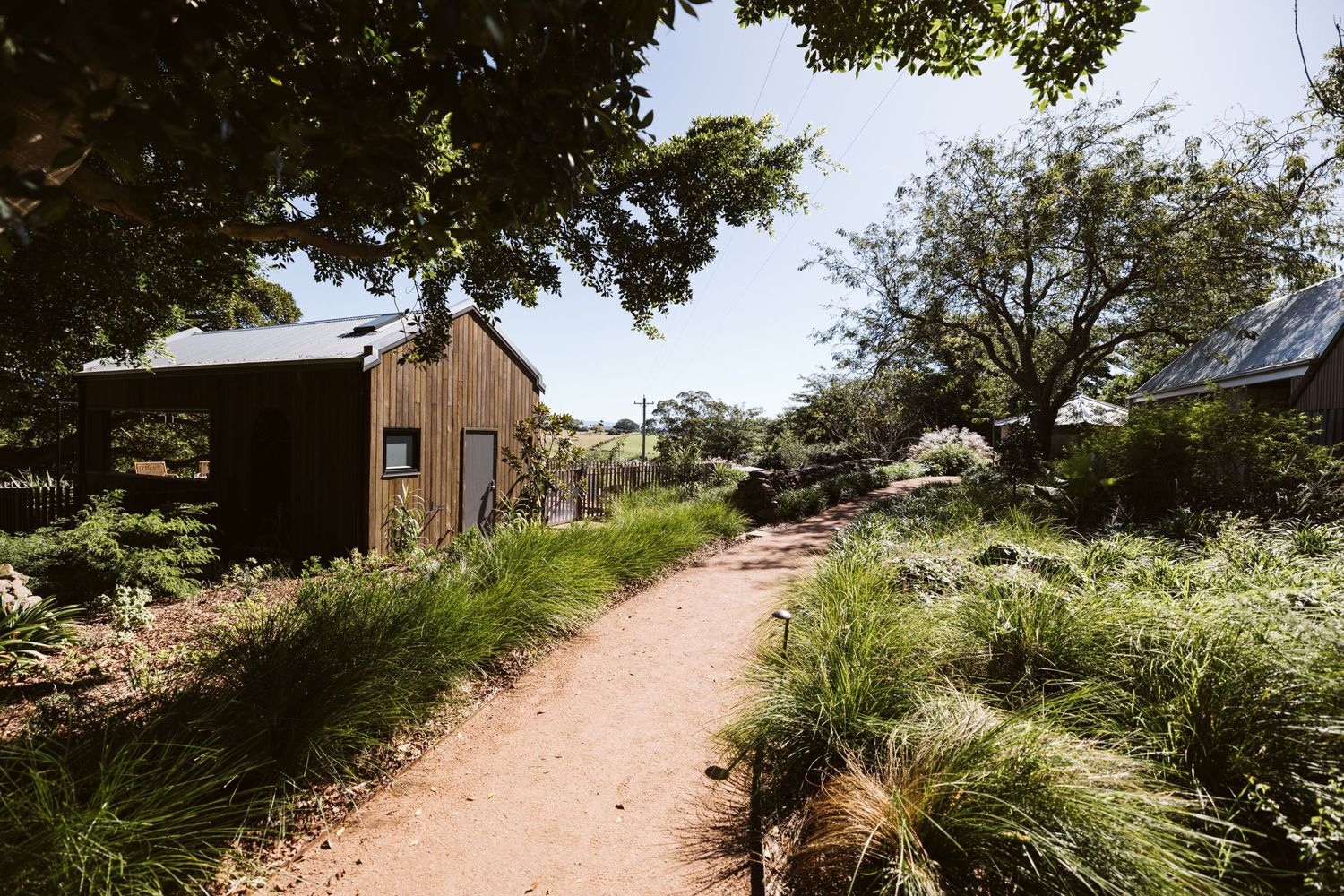 Rustic dirt path leads to a barn building surrounded by lush garden landscaping.
