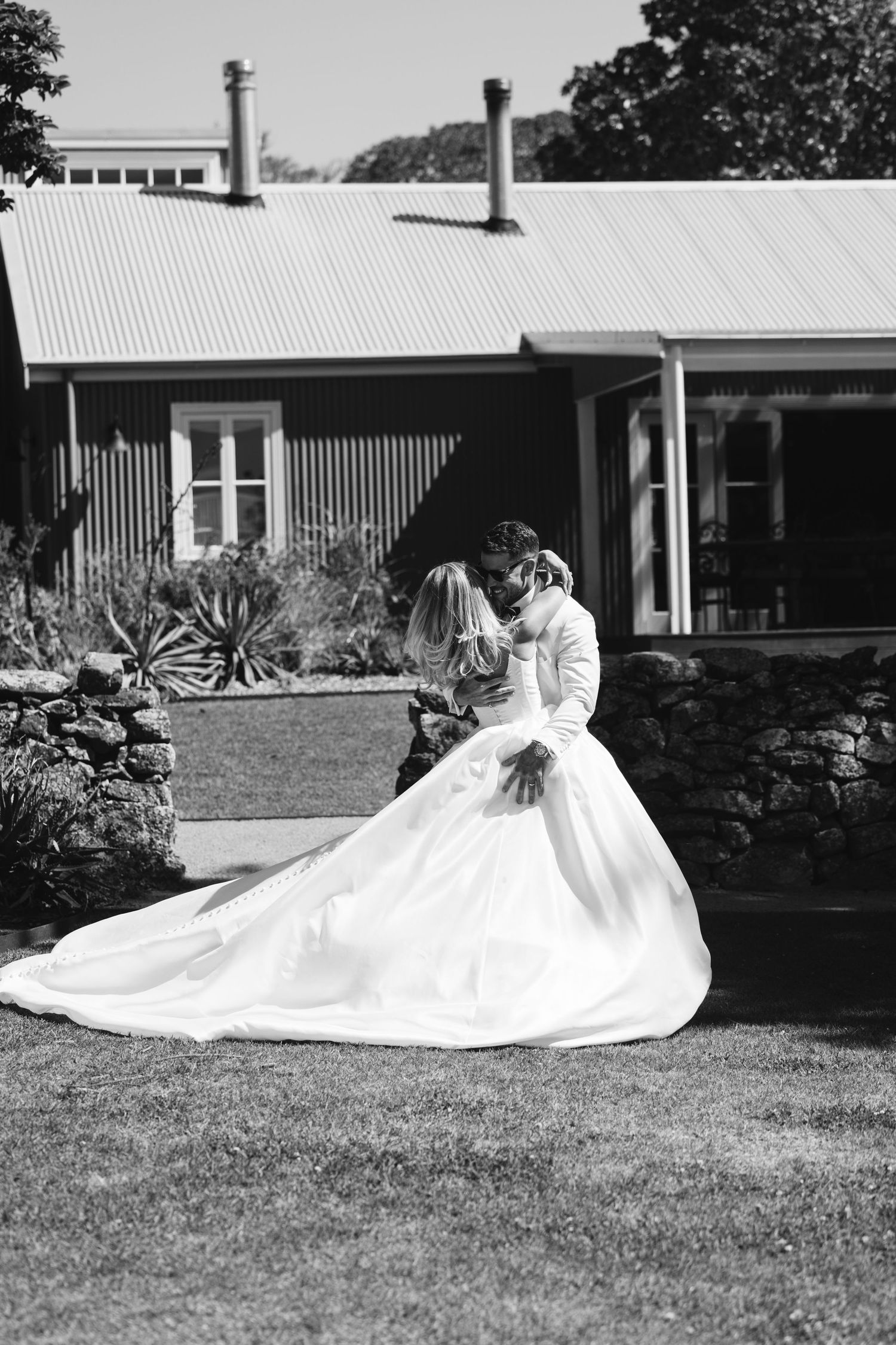 Black and white photo of a romantic dance pose outside a rustic building with metal roof.