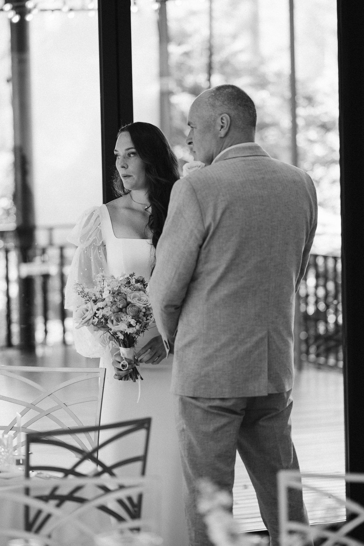 Black and white photo of a bride holding a bouquet standing with a man in a suit at a wedding ceremony.