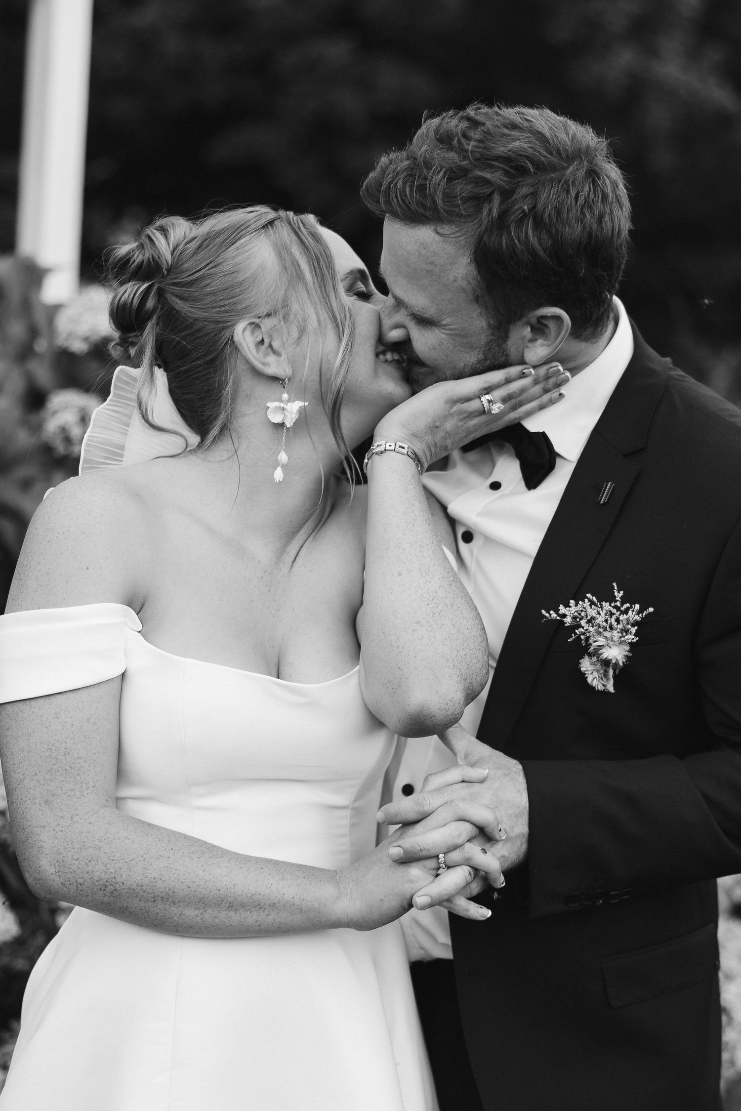 Black and white romantic portrait of newlyweds sharing an intimate kiss in formal wedding attire.