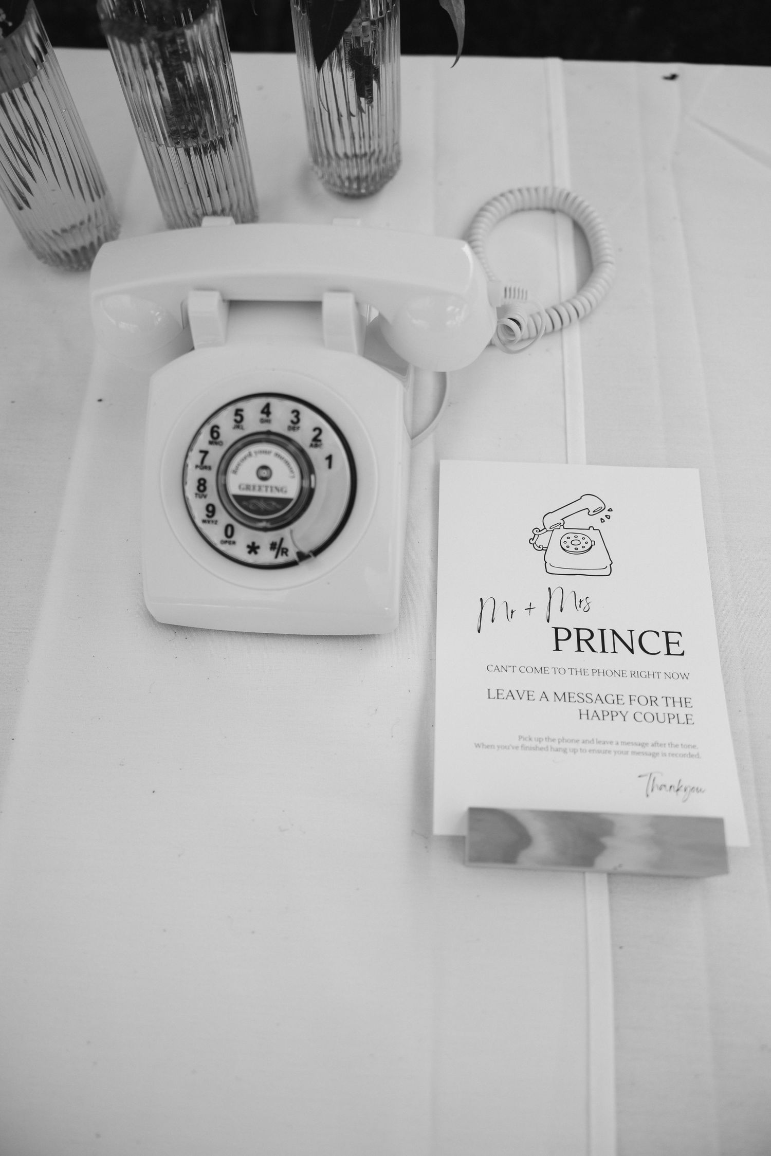 Vintage white rotary telephone next to Prince wedding venue information card on white surface.