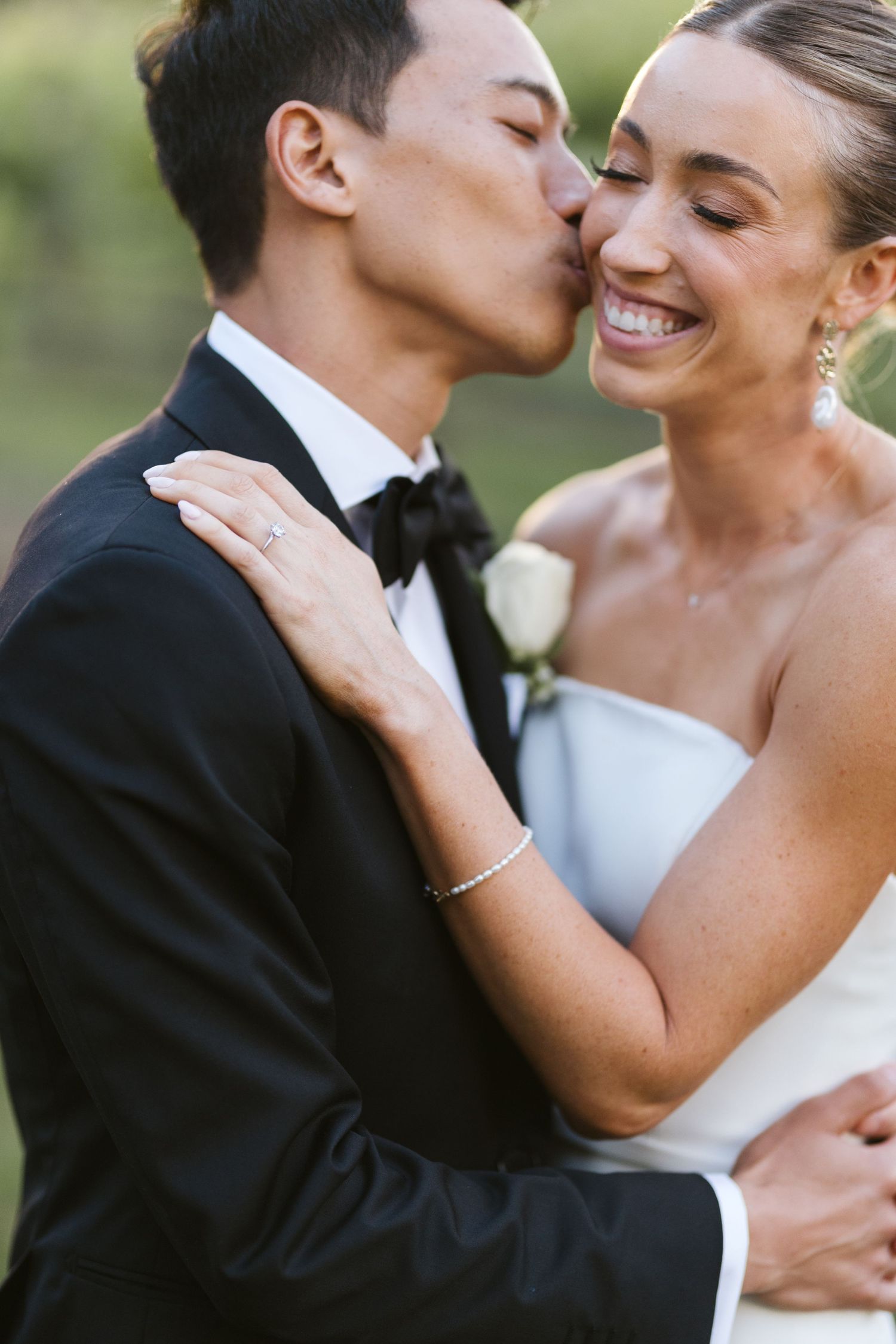 Intimate moment between newlyweds sharing a kiss outdoors.