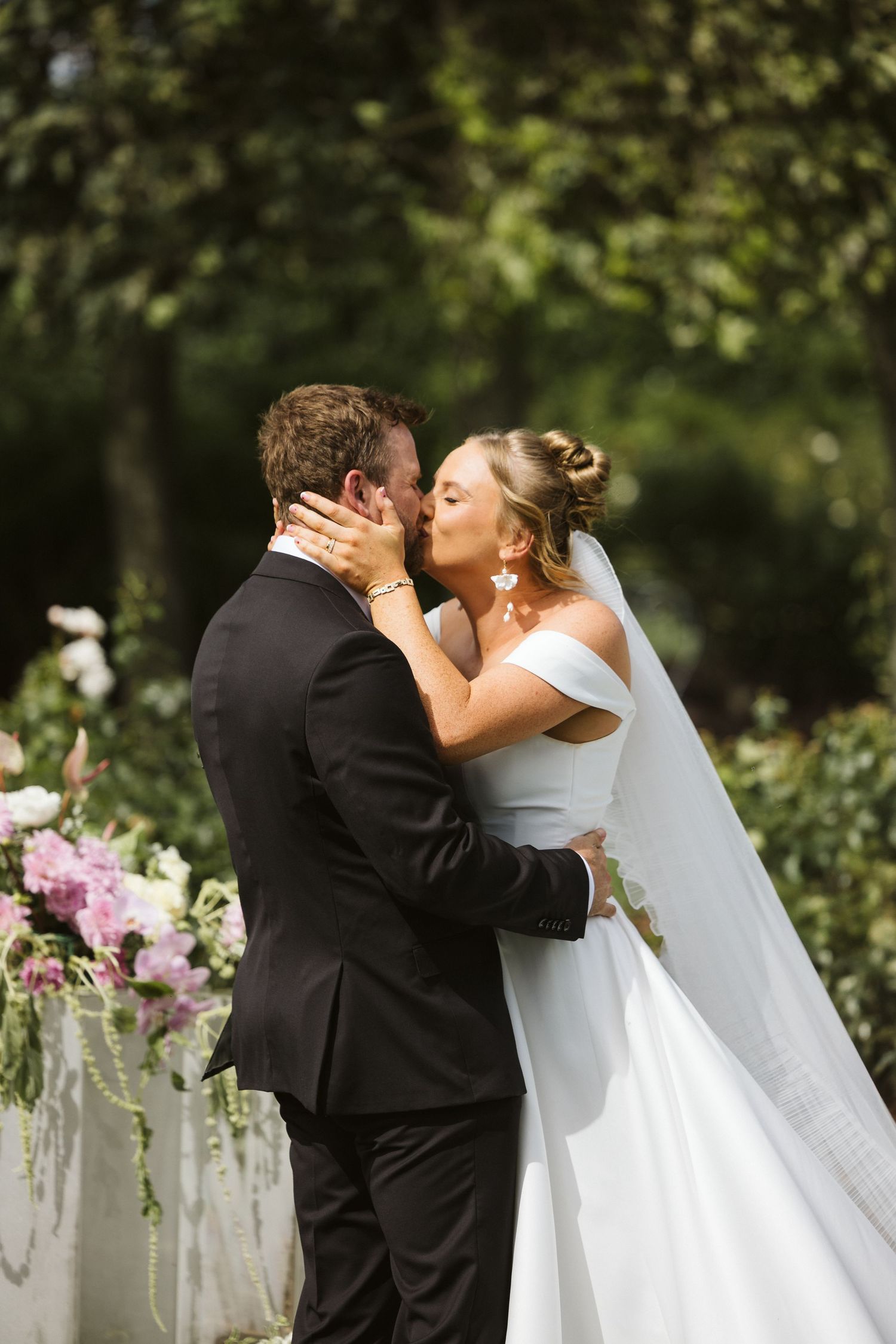 Tender moment between newlyweds with pink floral decorations in garden setting.
