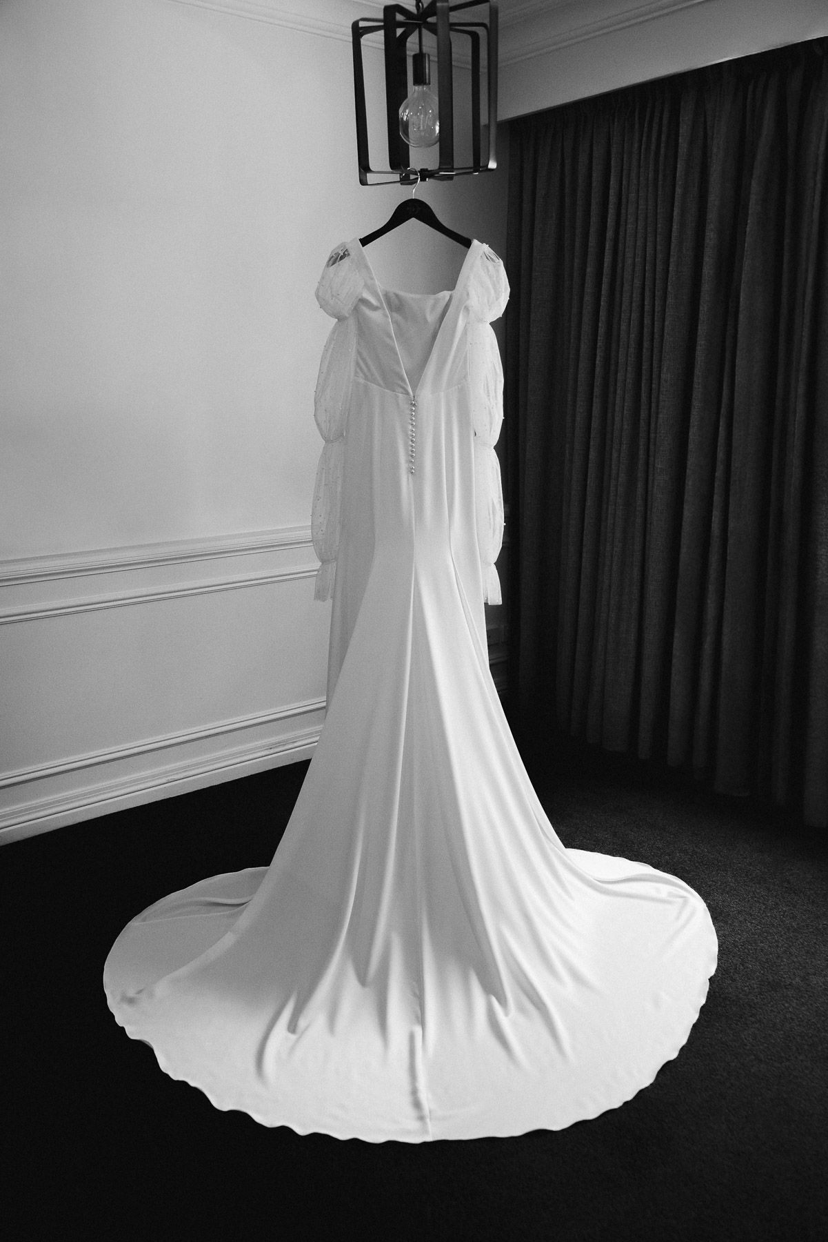 Elegant white wedding gown with long sleeves and cathedral train hanging on hanger, black and white photo.