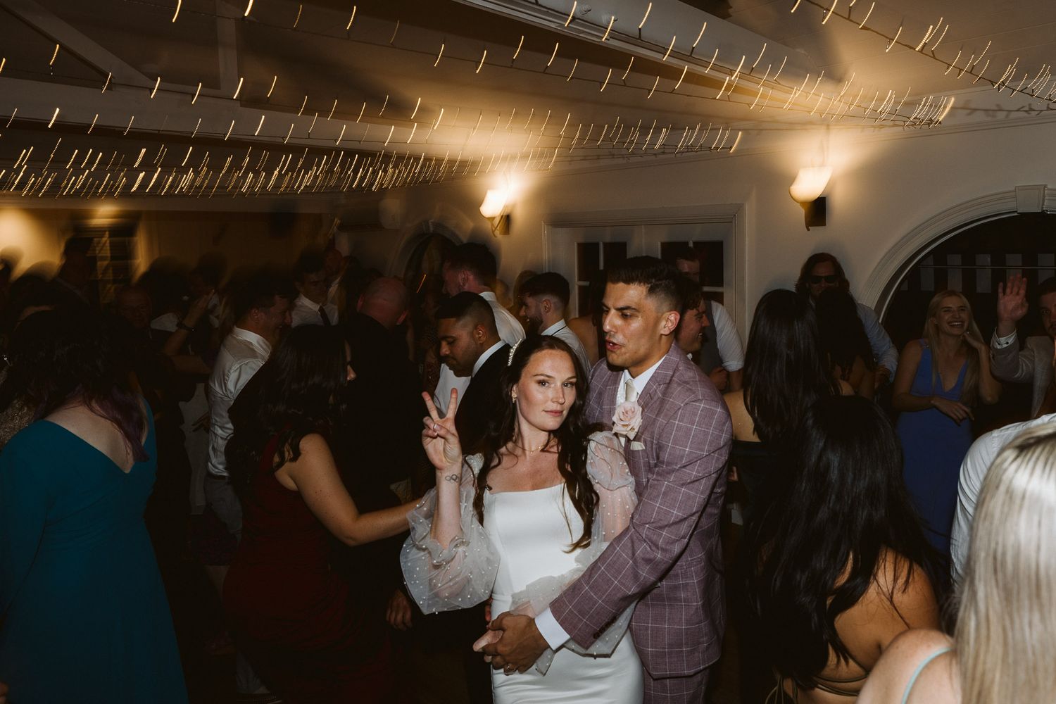 Bride and groom dancing together at elegant wedding reception with guests celebrating on the dance floor.