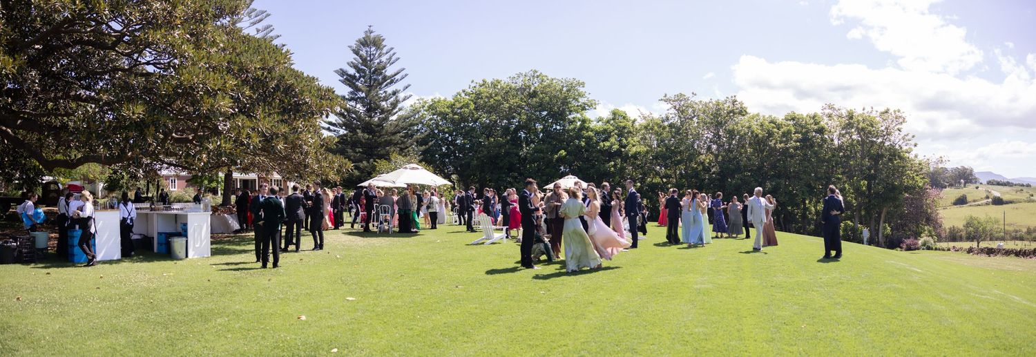 Panoramic view of outdoor wedding celebration with guests gathered under trees.