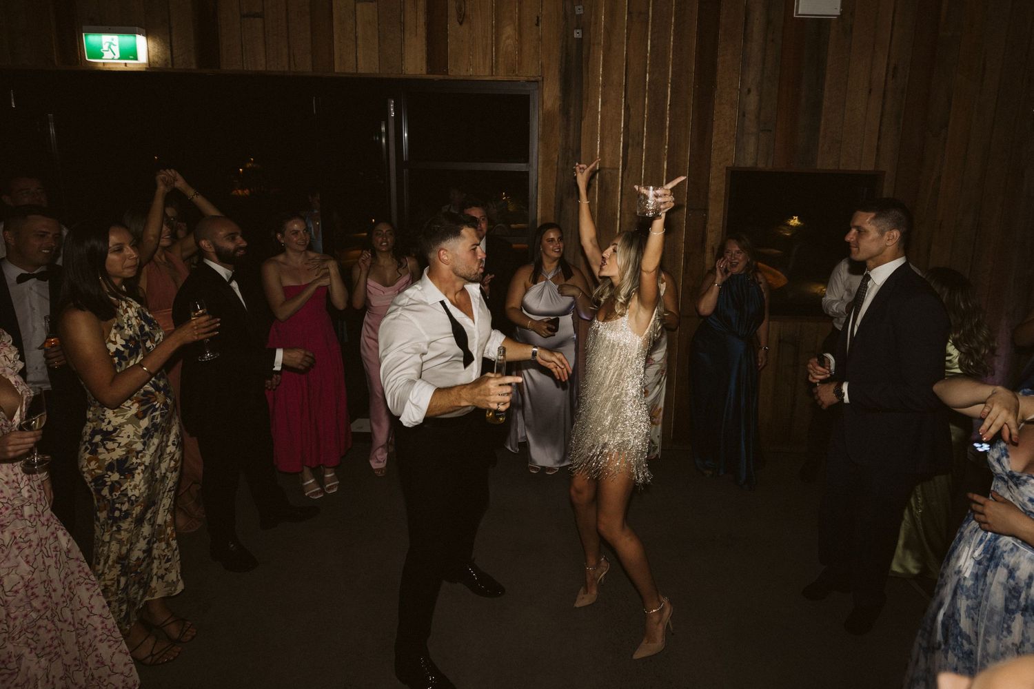 Wedding guests dance and celebrate in a rustic wooden venue.
