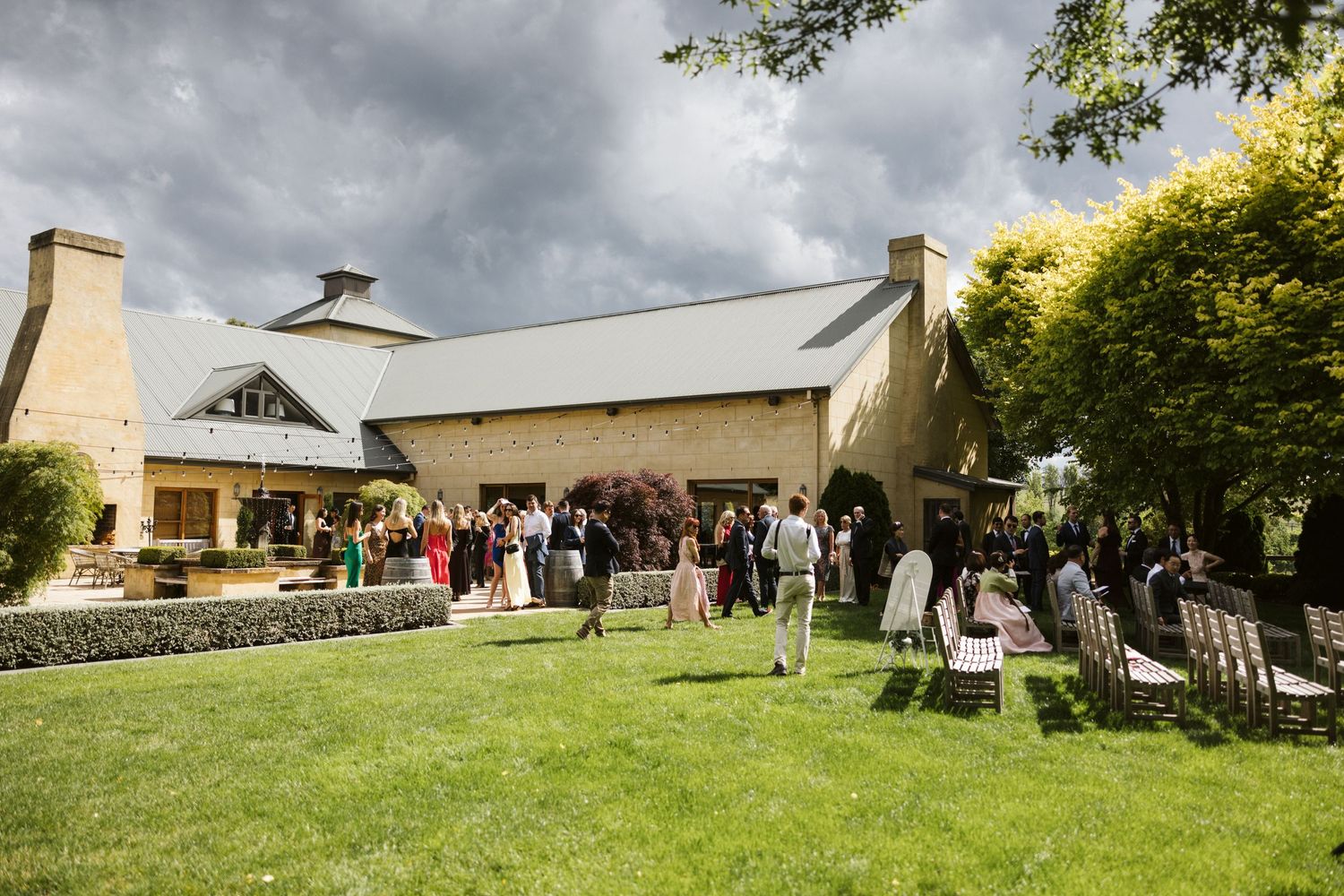 Wedding guests gathering outside a modern white reception venue with landscaped grounds.