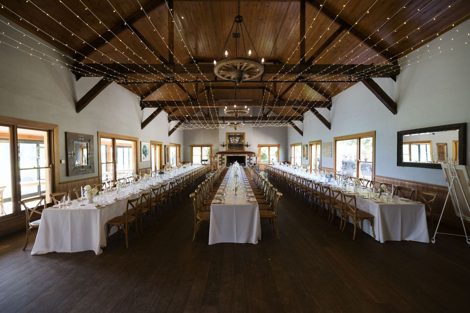 An elegant reception hall with long tables set under wooden beams and string lights.