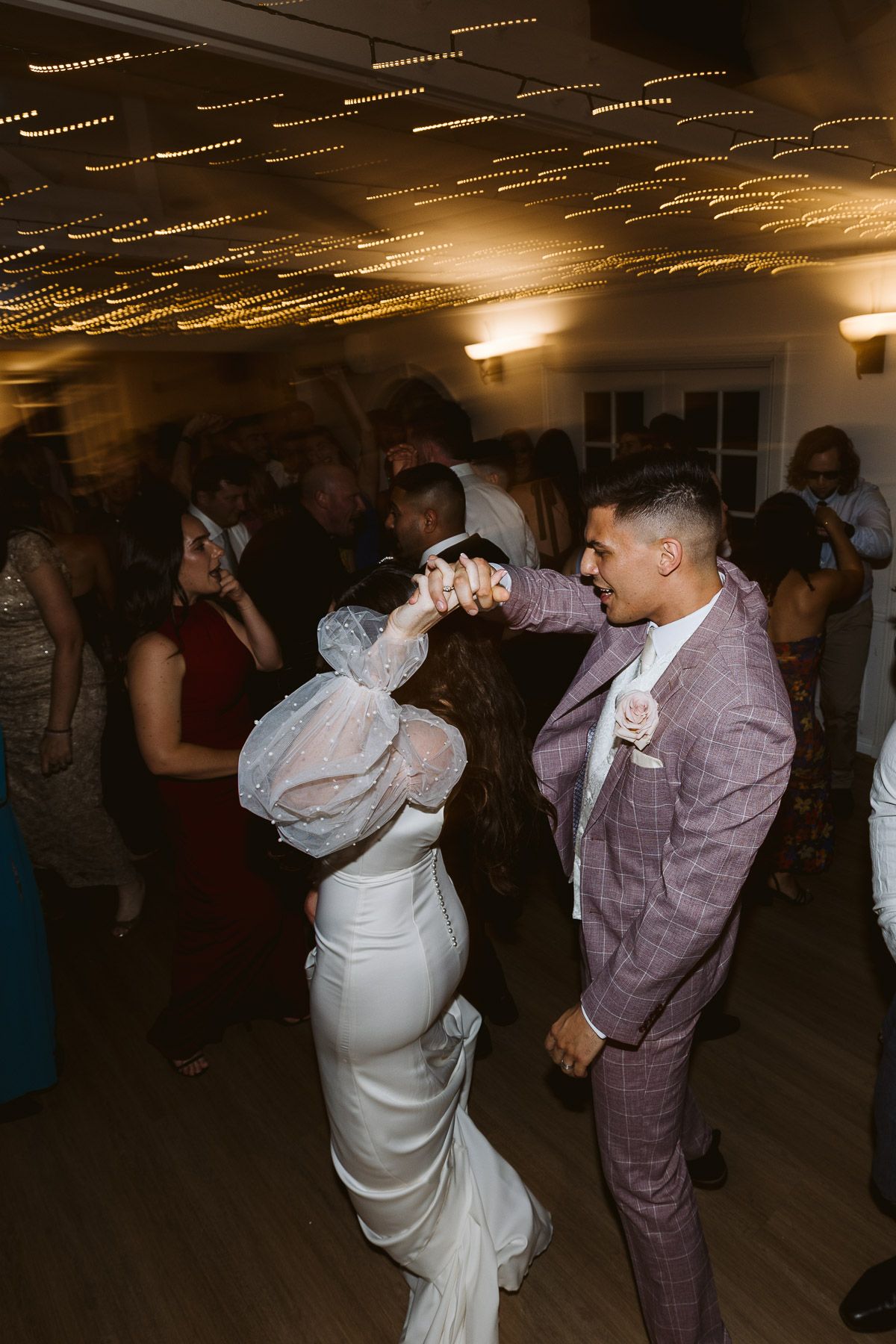 Bride in white gown and groom in pink suit share a romantic dance at their wedding reception.