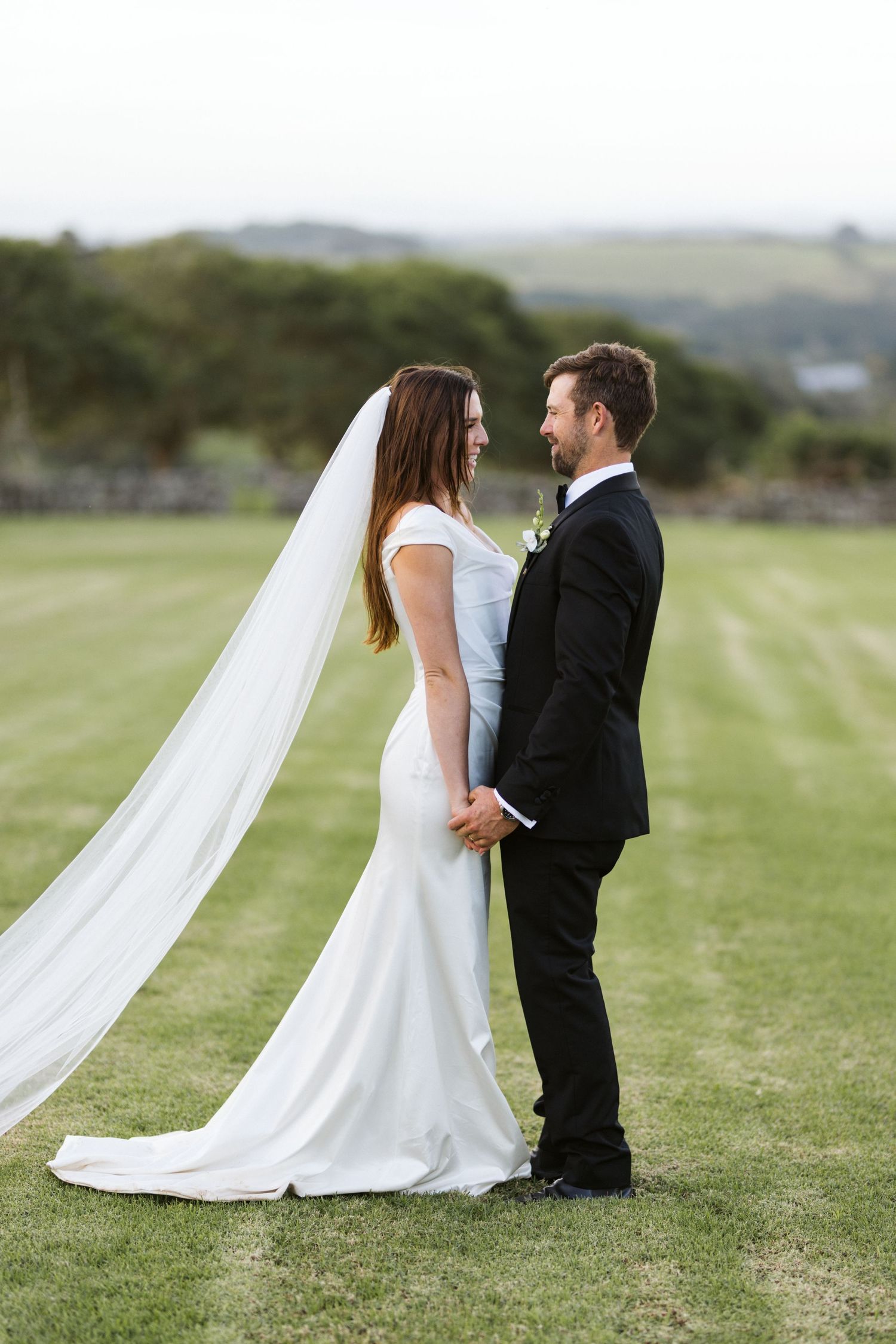 Elegant wedding portrait of a couple in formal attire standing close together on a green lawn.