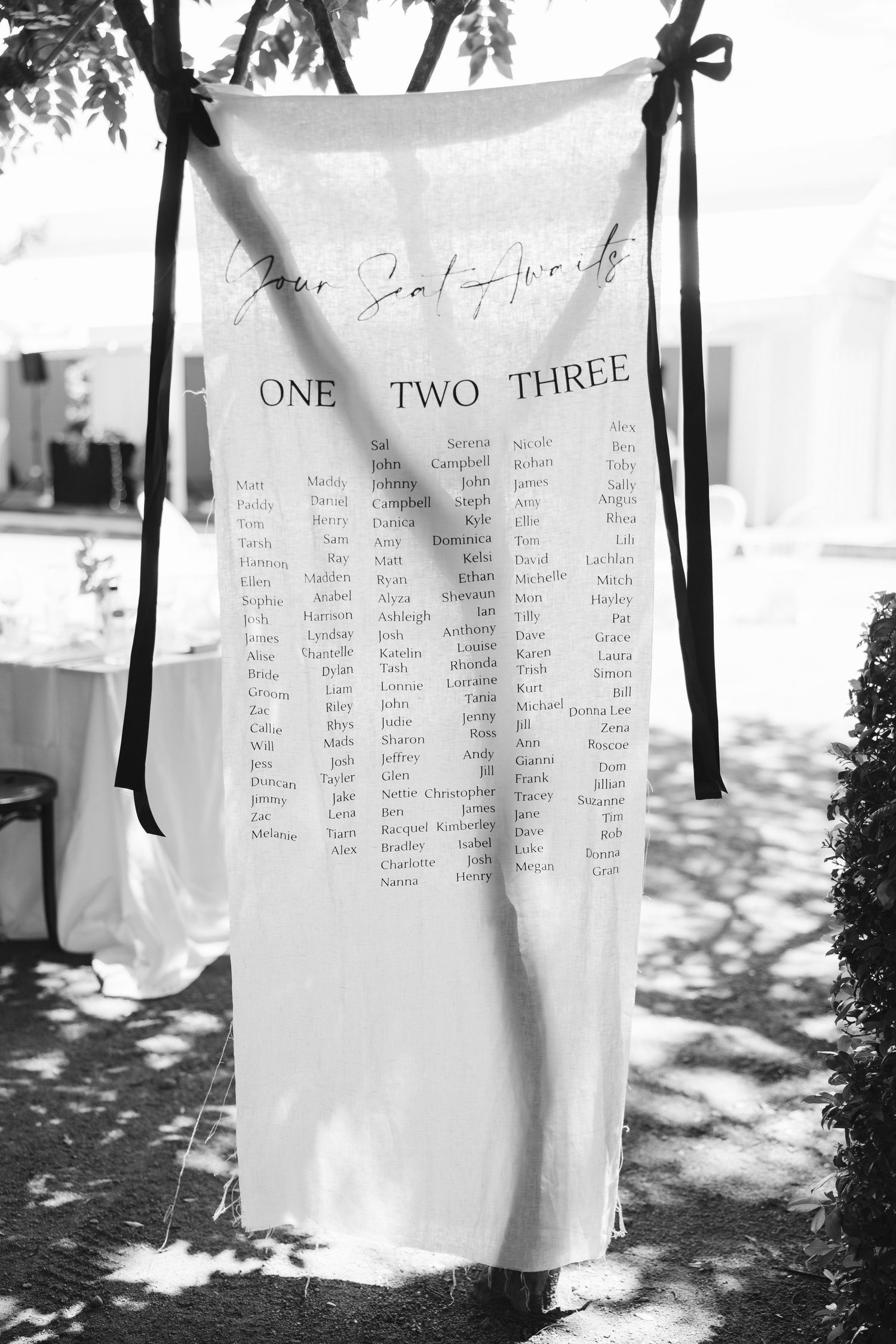 Black and white seating chart displayed on white fabric showing table assignments for guests.