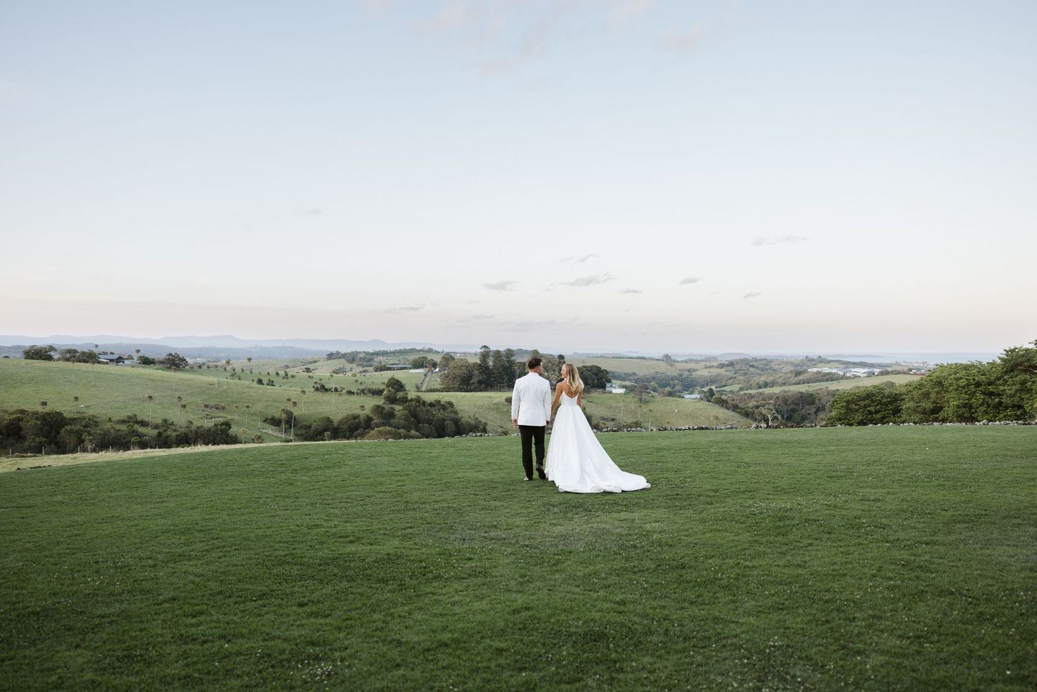 A bride and groom standing together on a grassy hilltop with rolling hills in the background.