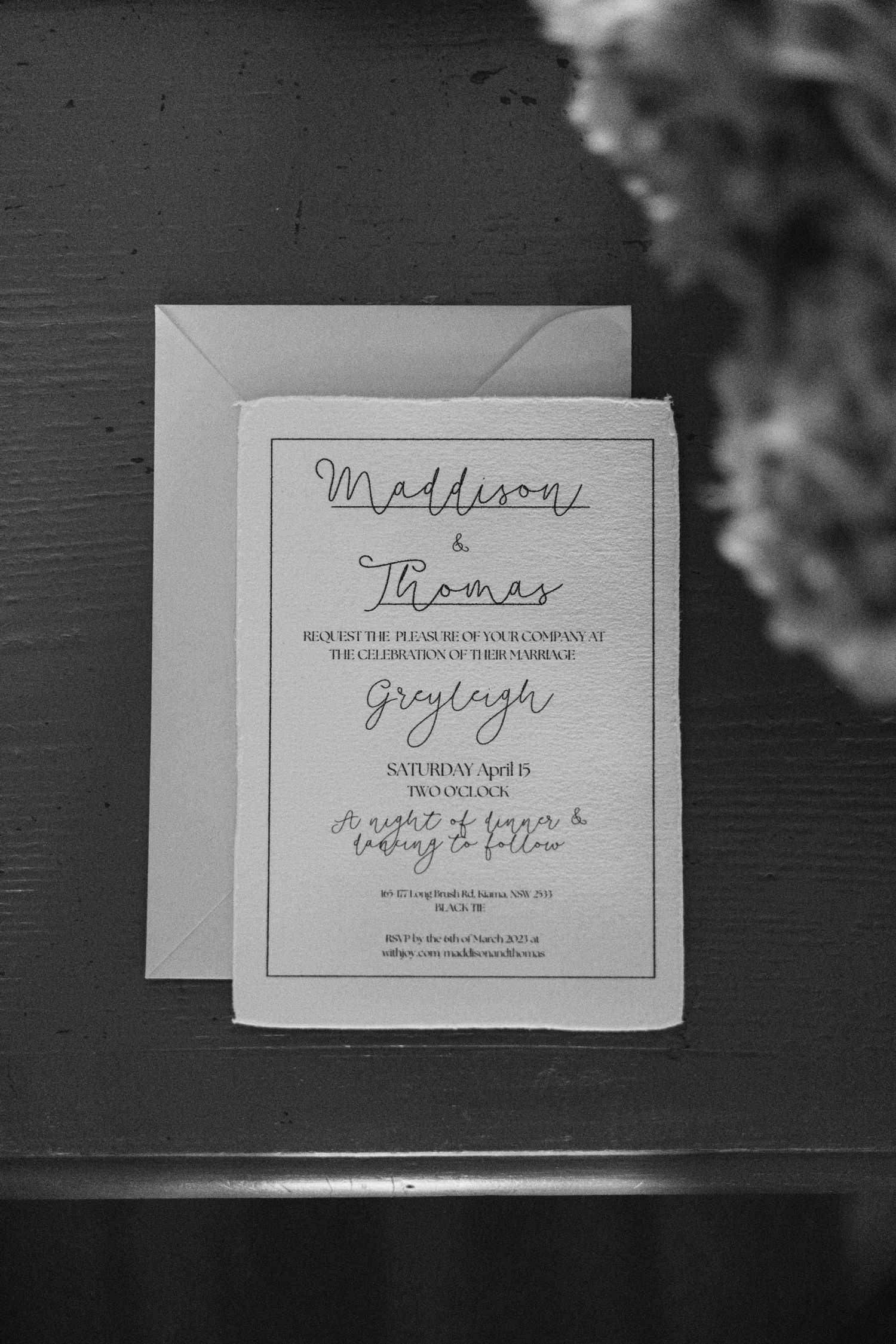 Black and white wedding invitation with elegant script font on dark surface.
