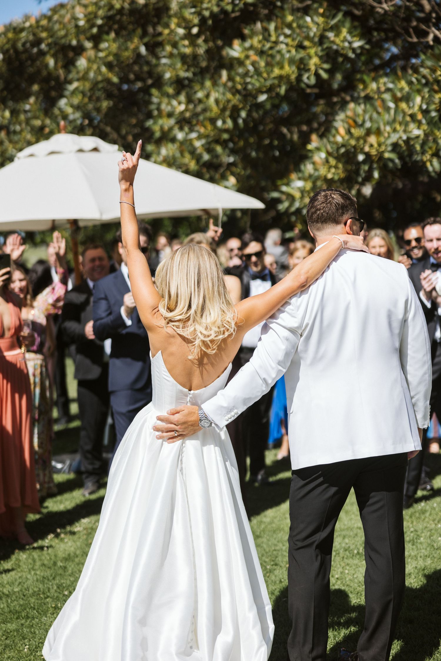 Celebratory moment at outdoor wedding reception with crowd of guests and white umbrellas.