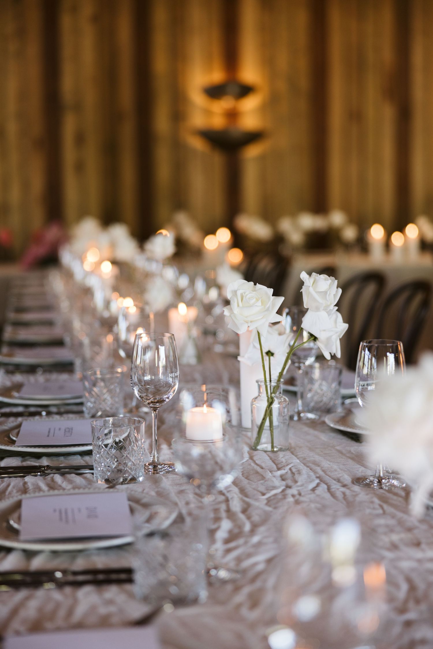 White roses in glass vases line a wedding table with glowing candles and crystal glassware.