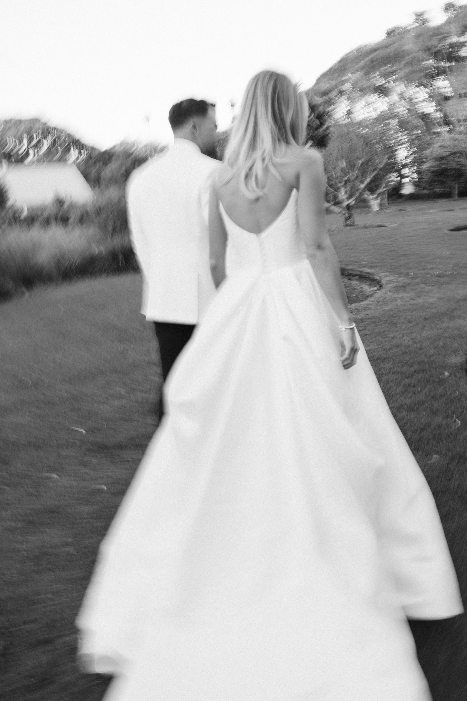 Black and white photo of couple walking against scenic hillside backdrop.