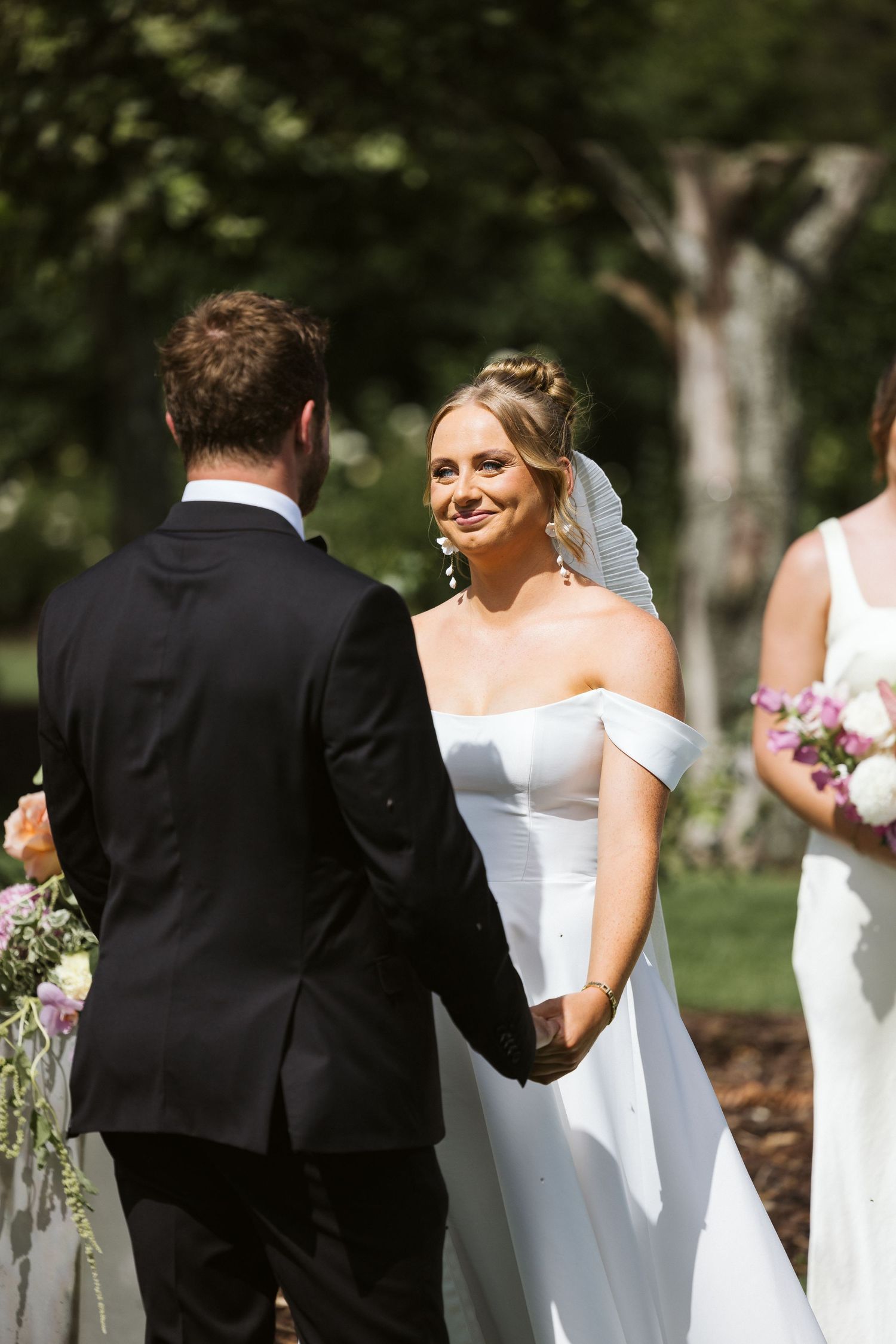 Wedding couple holds hands during their outdoor garden ceremony surrounded by greenery.