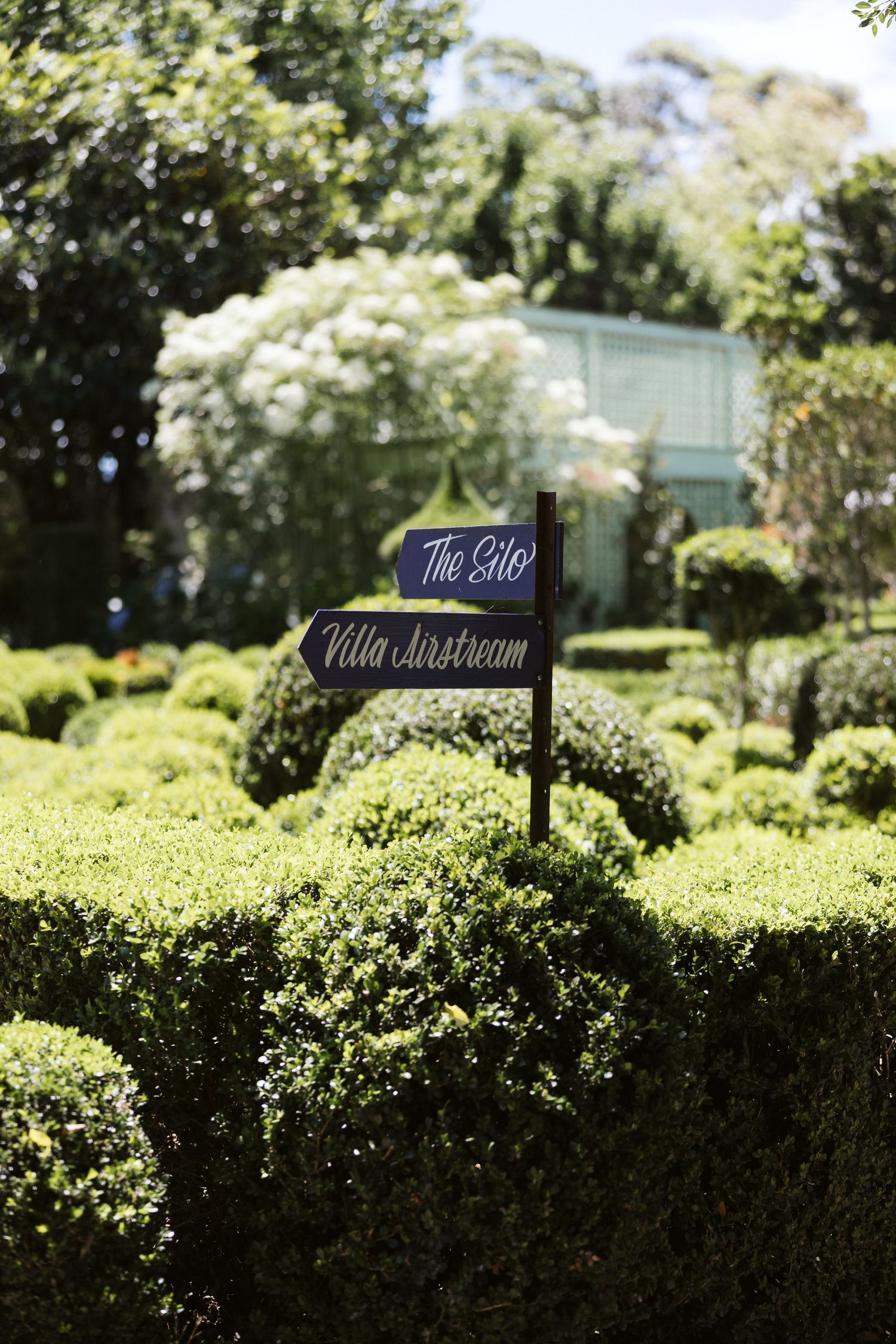 Garden directional sign reading 'The Gift Villa Bathroom' among neatly trimmed hedges.