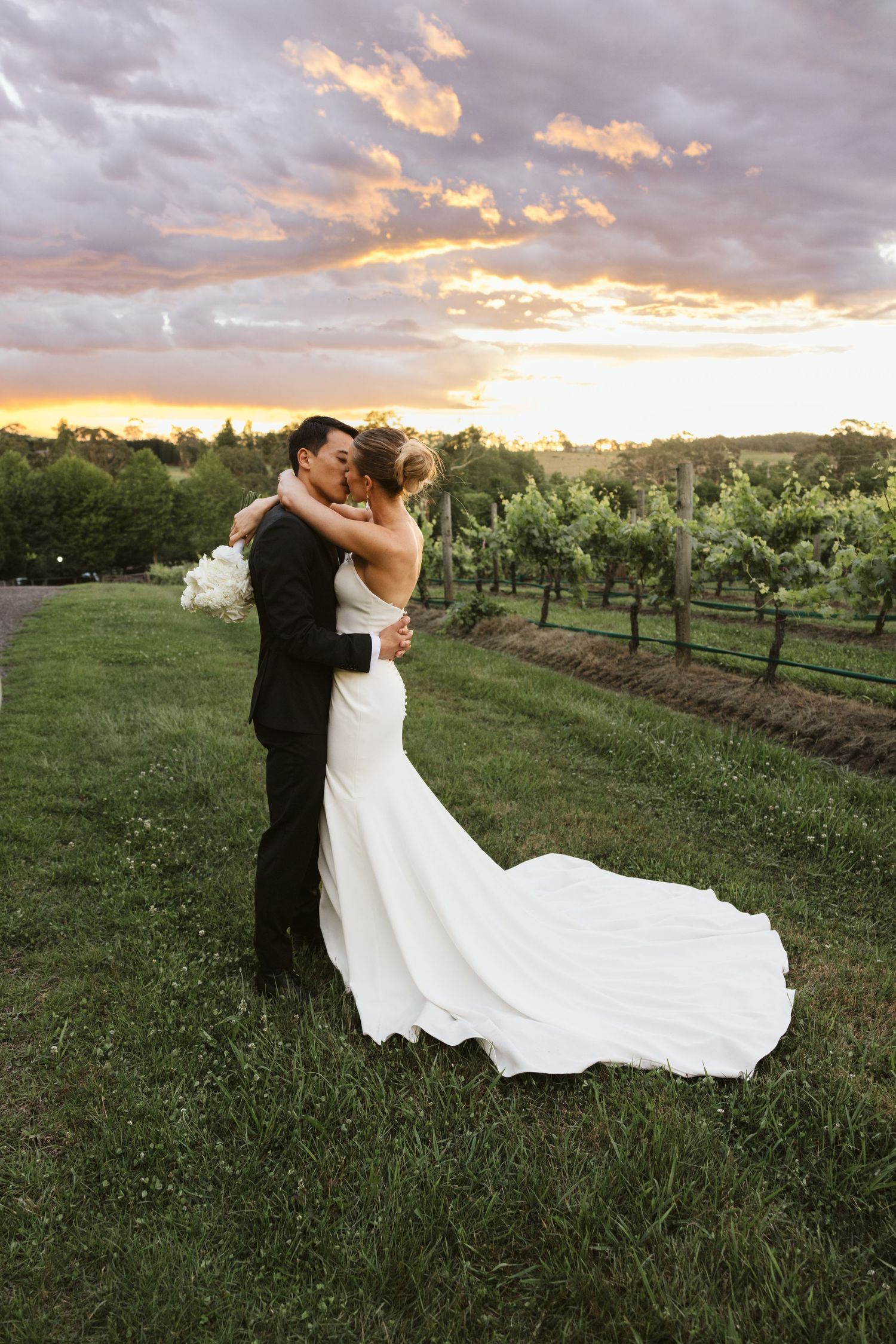 Romantic sunset portrait of newlyweds embracing in vineyard with dramatic sky.