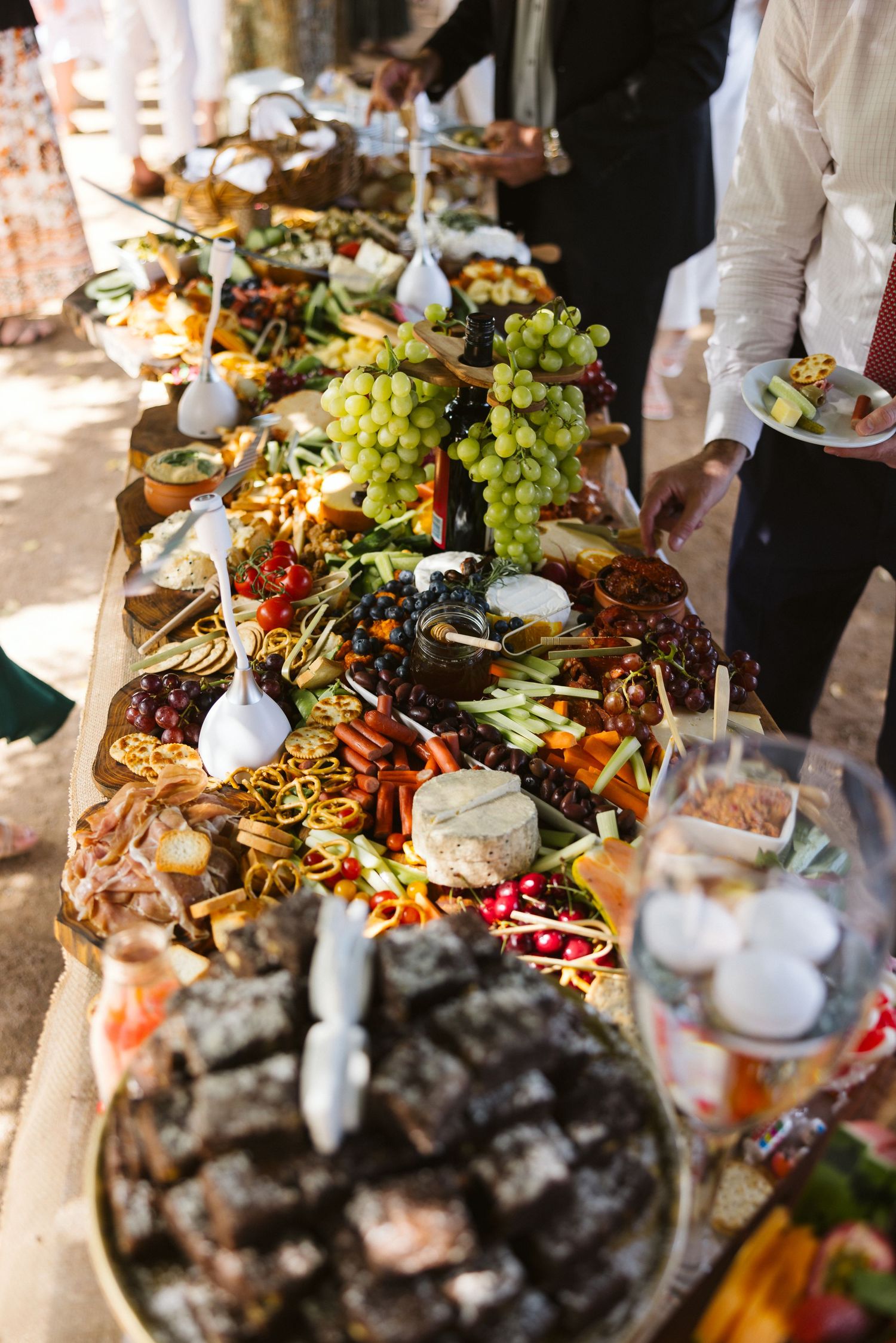 Elegant wedding buffet table with grapes, meats, cheeses and appetizers on a rustic wood surface.