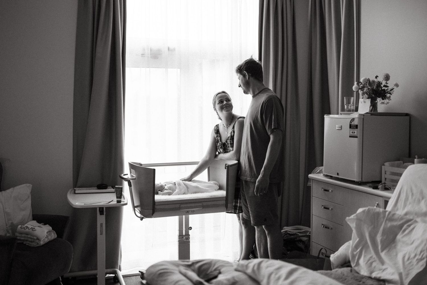 Black and white image of new parents lovingly looking at newborn in hospital room.