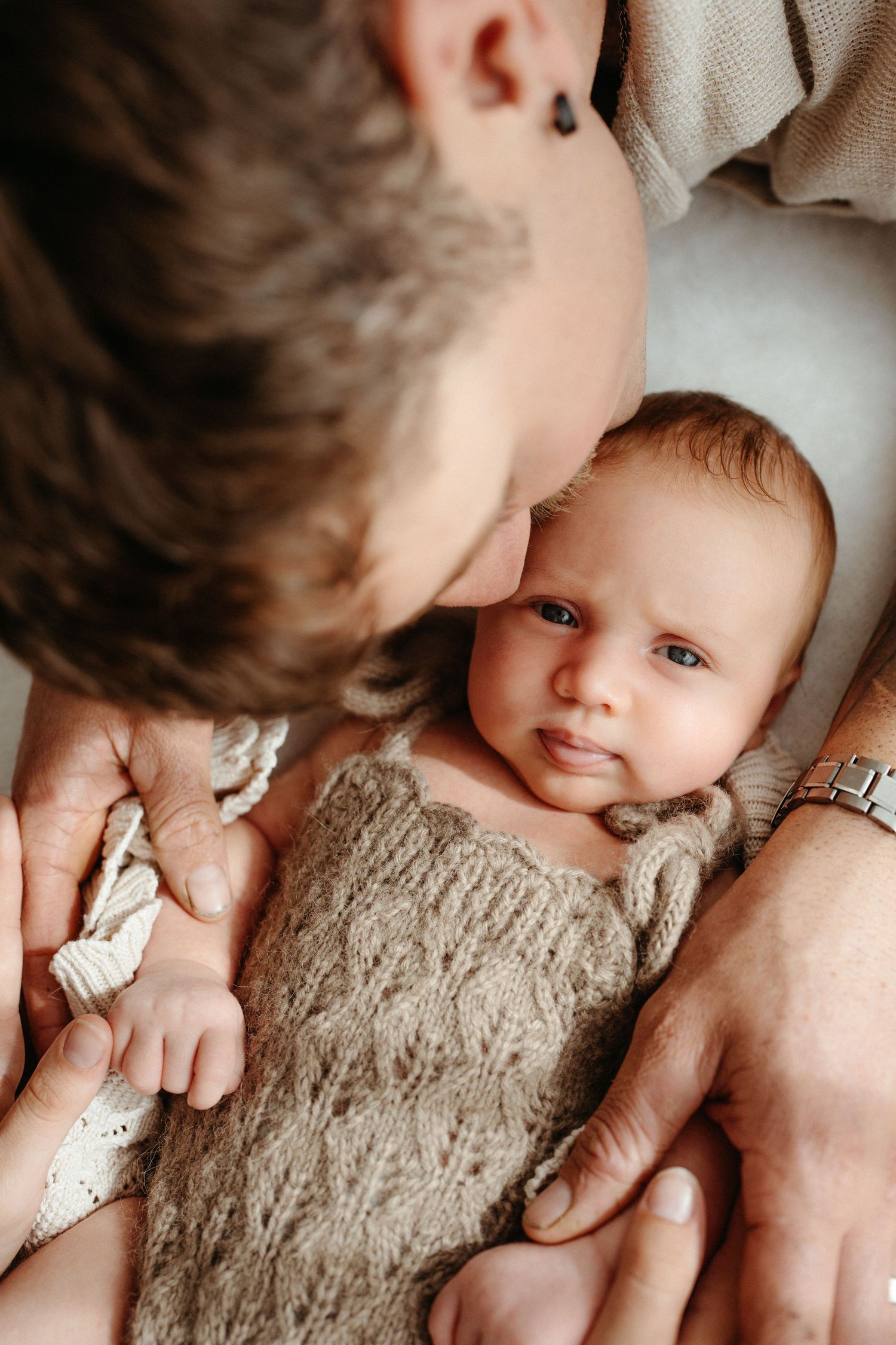 A father tenderly kisses his newborn baby wrapped in a cozy knit blanket, capturing a heartwarming bonding moment.