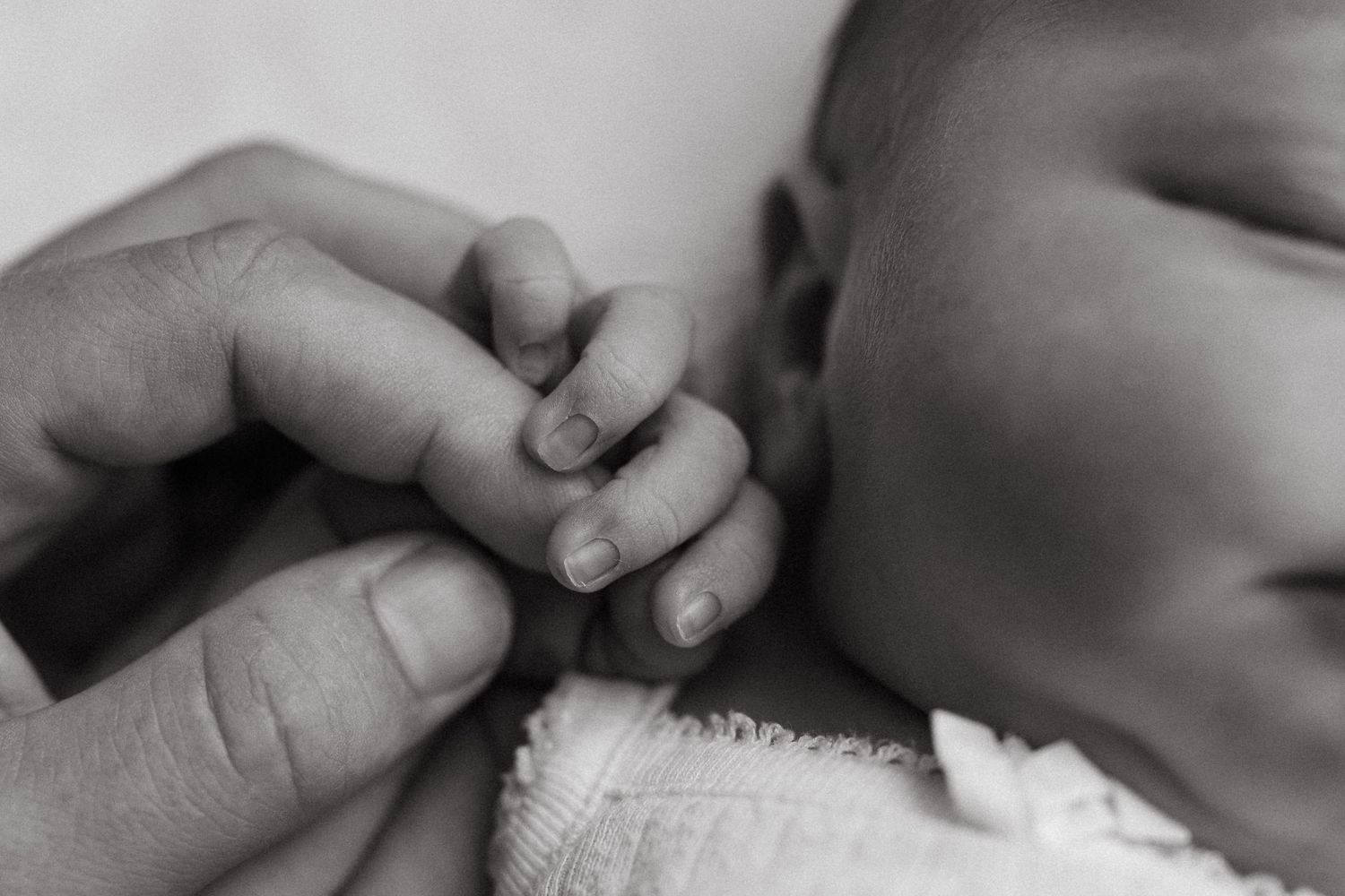 Black and white close-up of a newborn gripping an adult's finger.