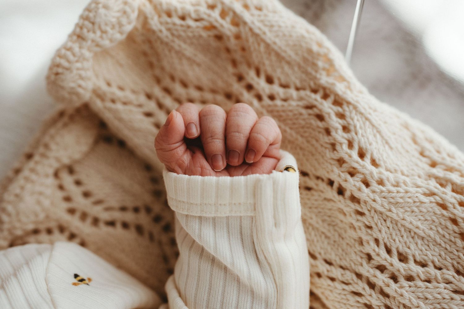 Close-up of a newborn baby's tiny fist wrapped in a cream knit blanket.