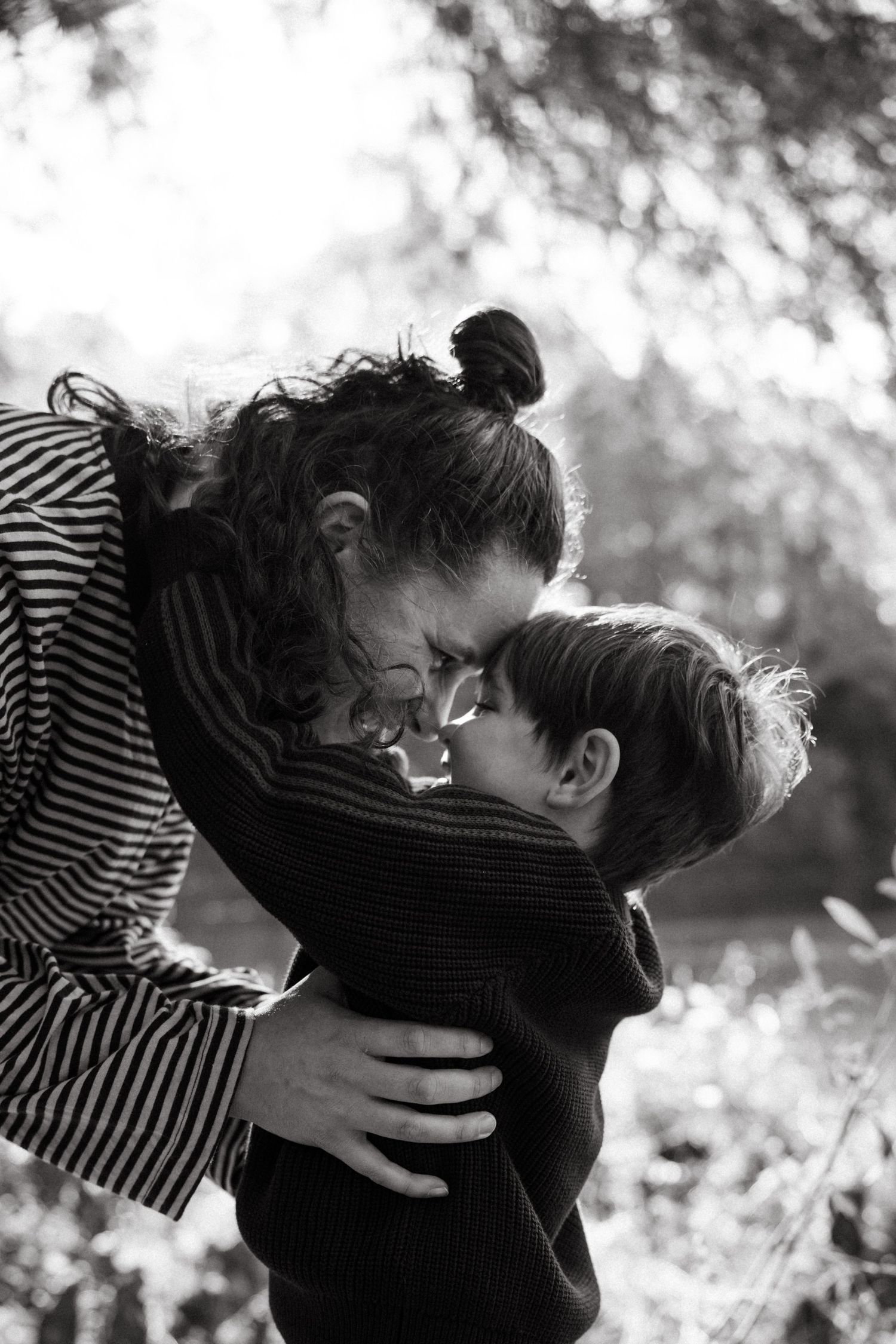Black and white photo of smiling mother and young son touching foreheads in tender outdoor embrace.