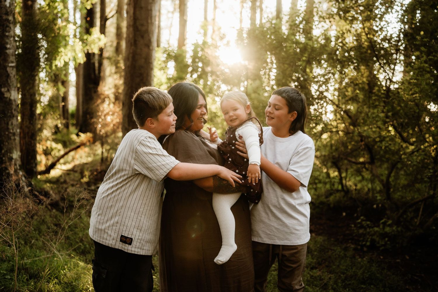 Family of four sharing a joyful moment in a sunlit forest, with warm golden light filtering through the trees.