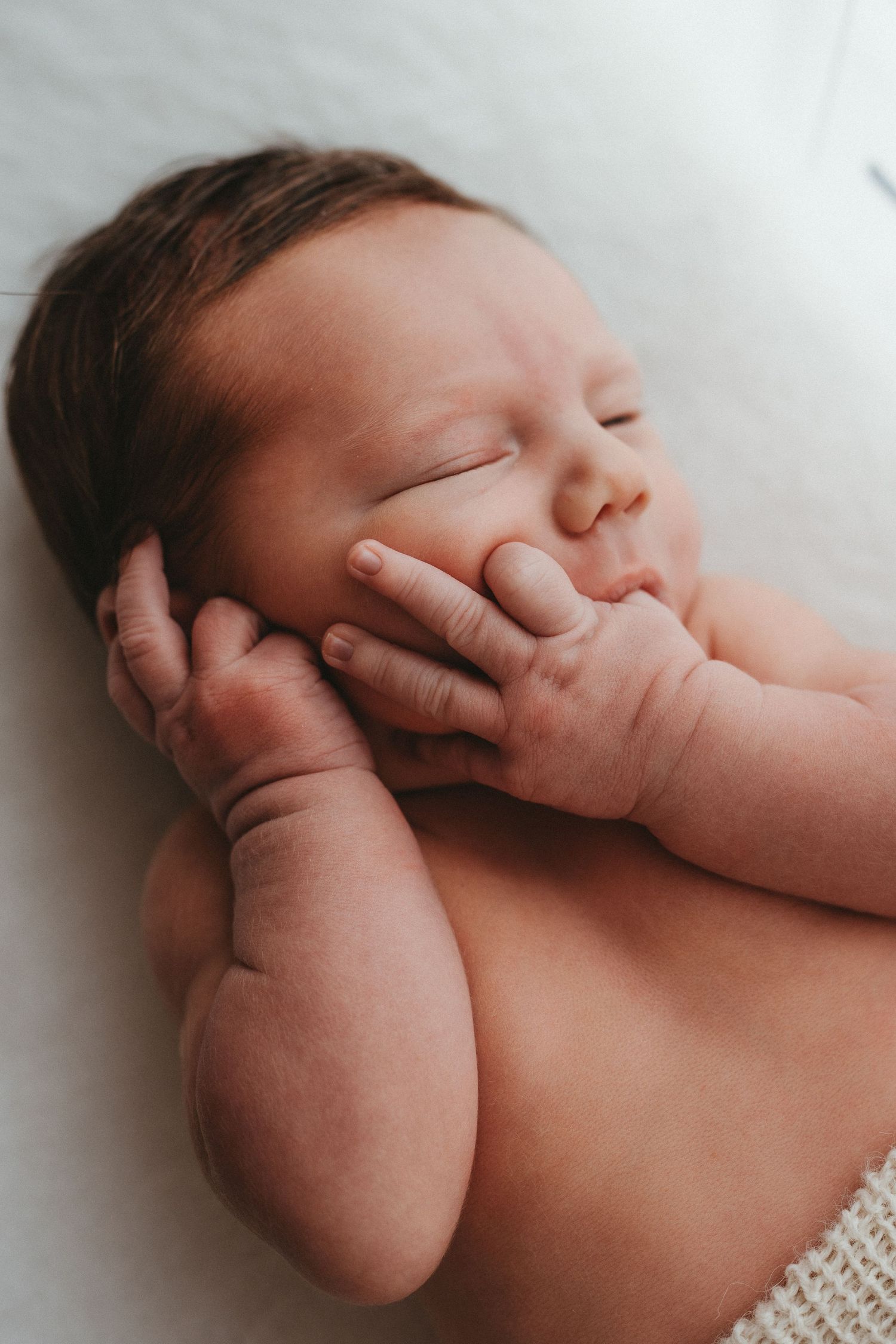 Close-up of a serene newborn baby resting with hands tucked against cheeks.