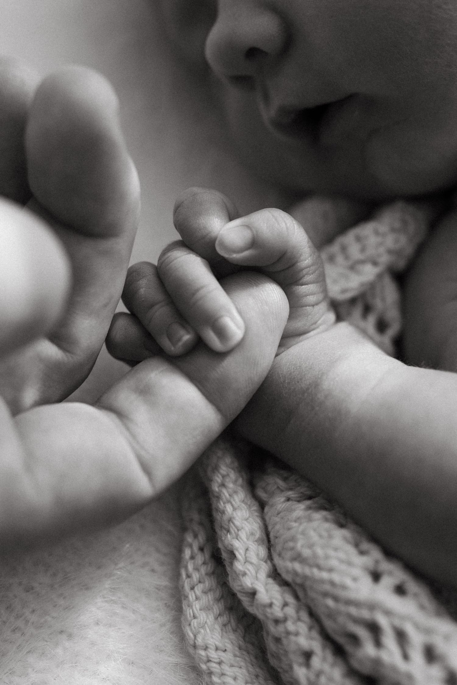 Black and white close-up of a newborn baby gripping a parent's finger.