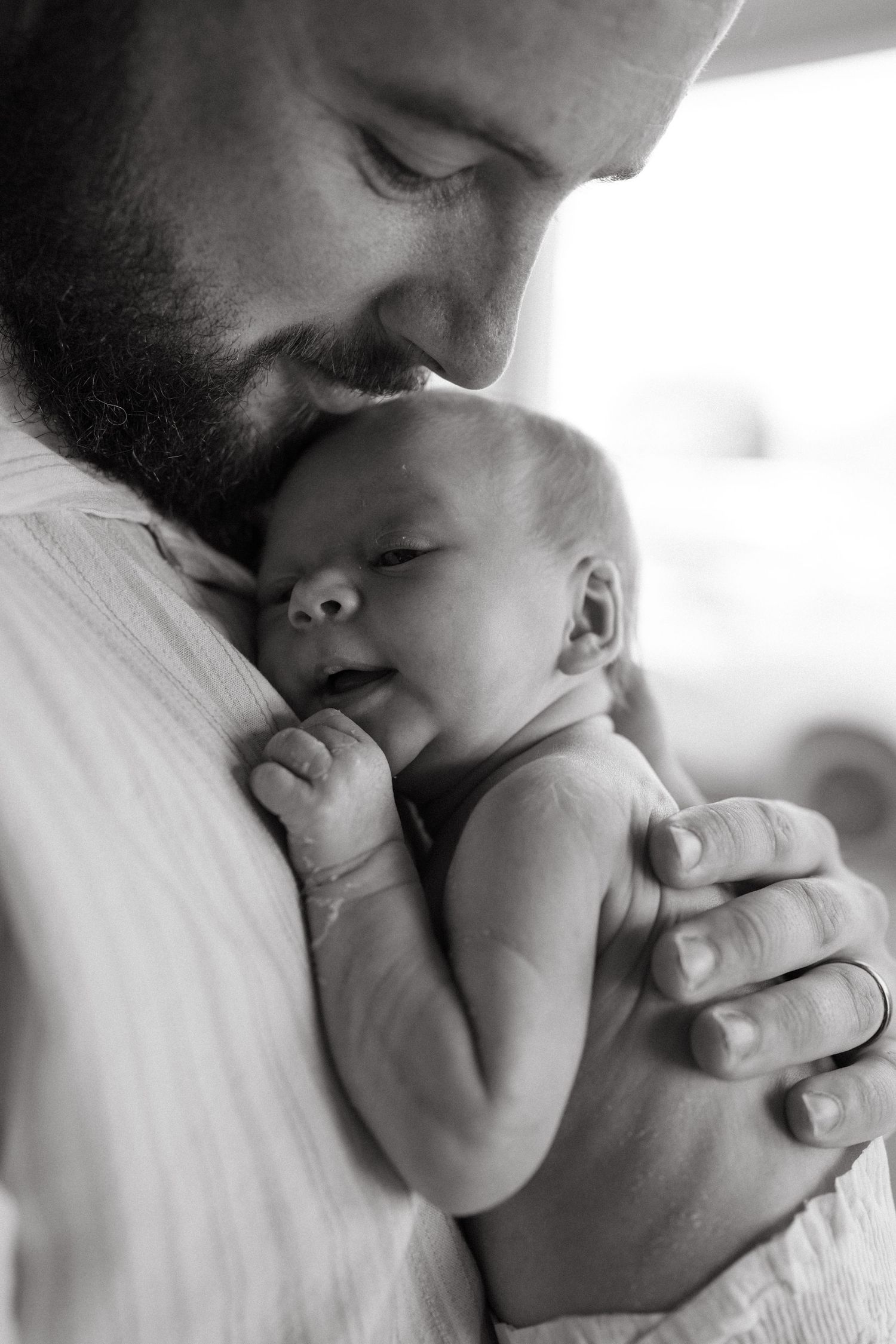 Black and white photo of a bearded father tenderly holding and kissing his sleeping newborn baby.