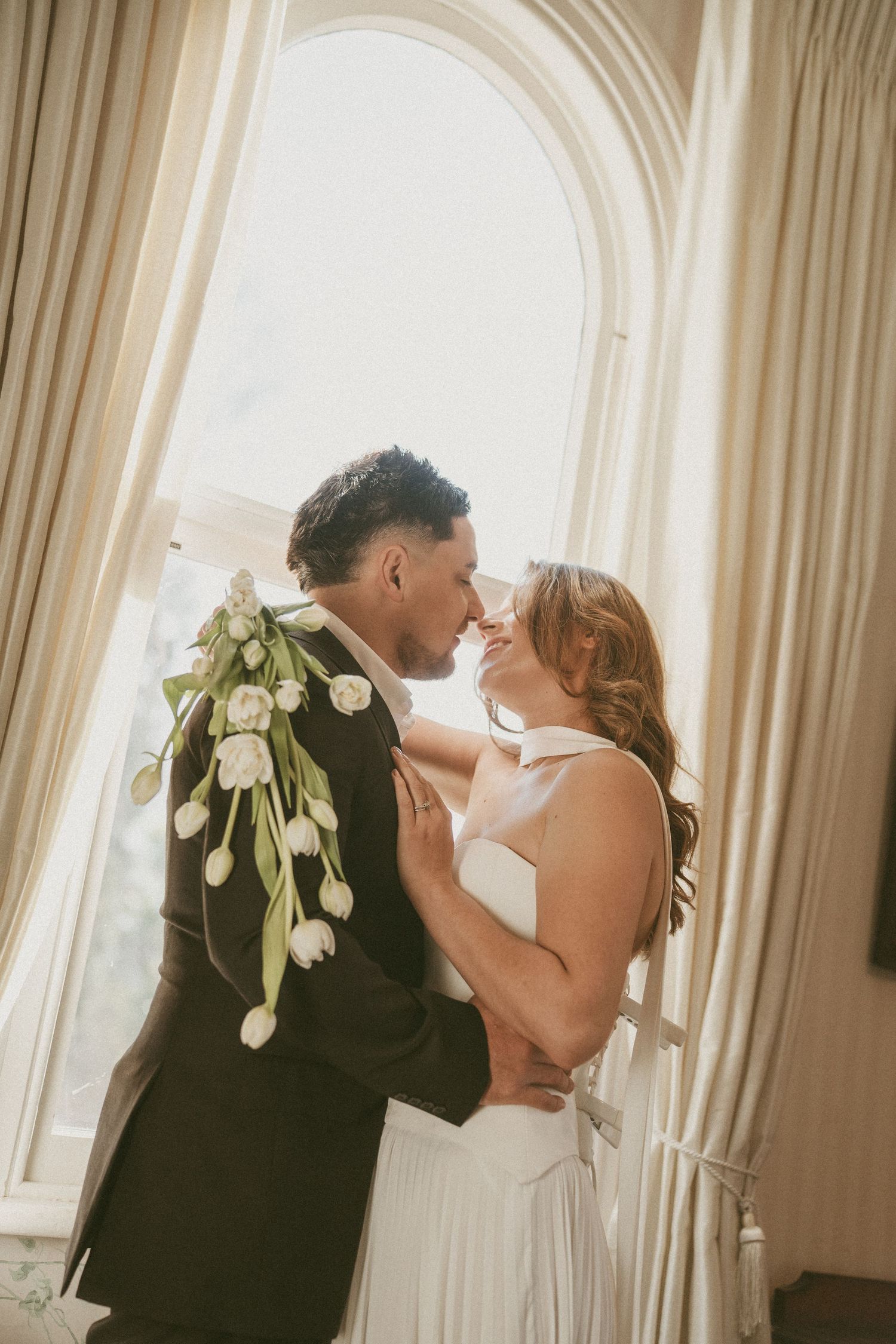Katie Charlotte Photography Bride and groom share a romantic almost-kiss in front of an arched window.