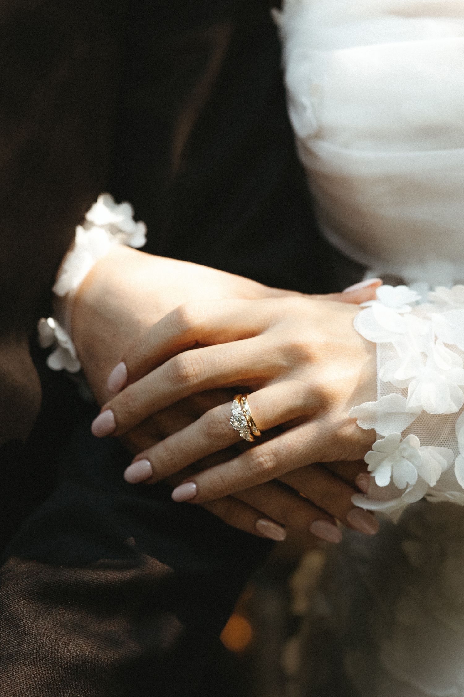 Close-up of bride's hands wearing a gold diamond wedding ring resting on white floral dress.