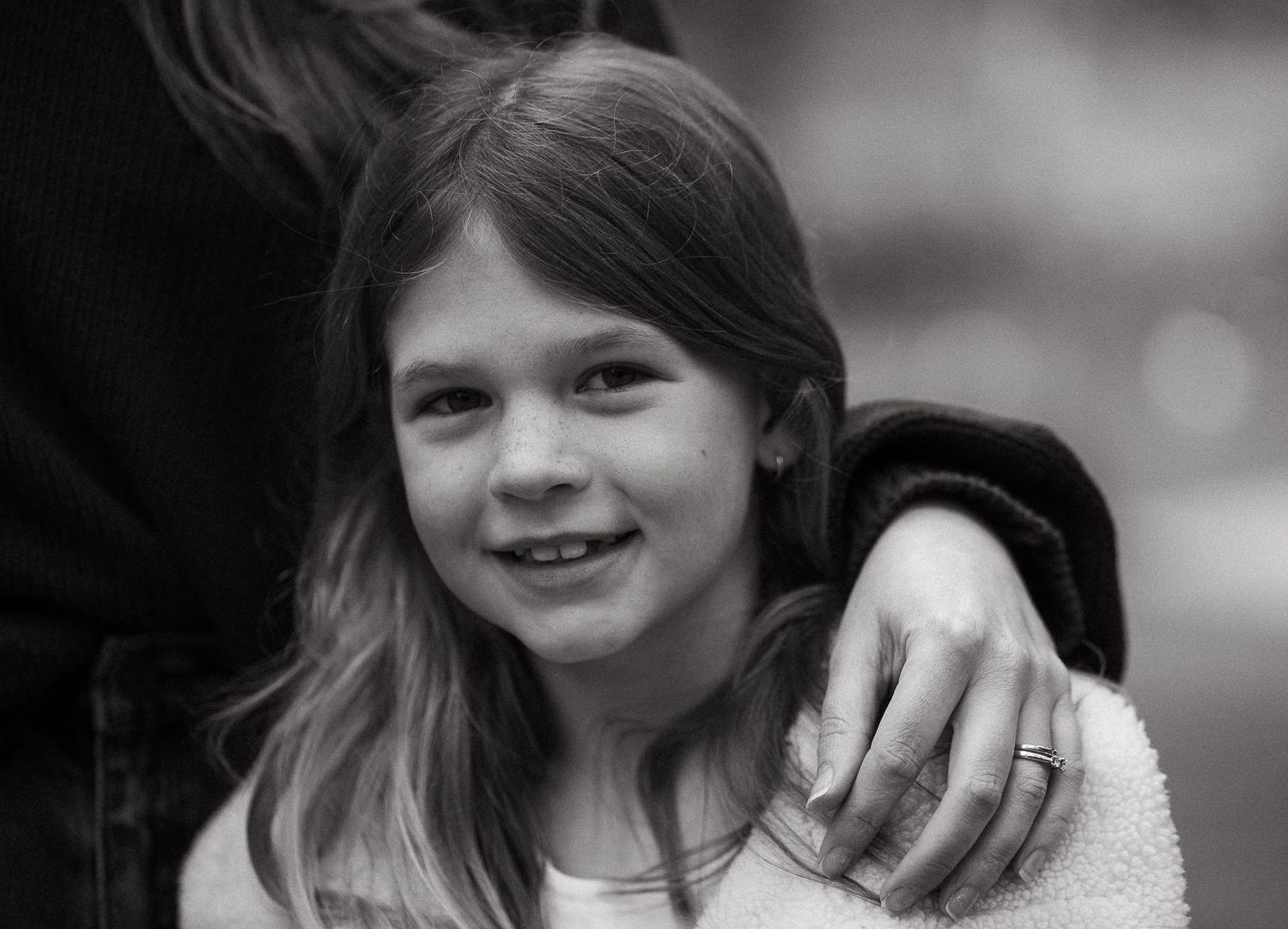 Black and white portrait of a smiling young girl with long hair outdoors.