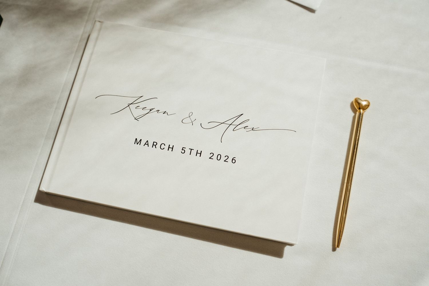 Elegant wedding guest book with gold pen reading Kayla and Alex, March 5th 2026.
