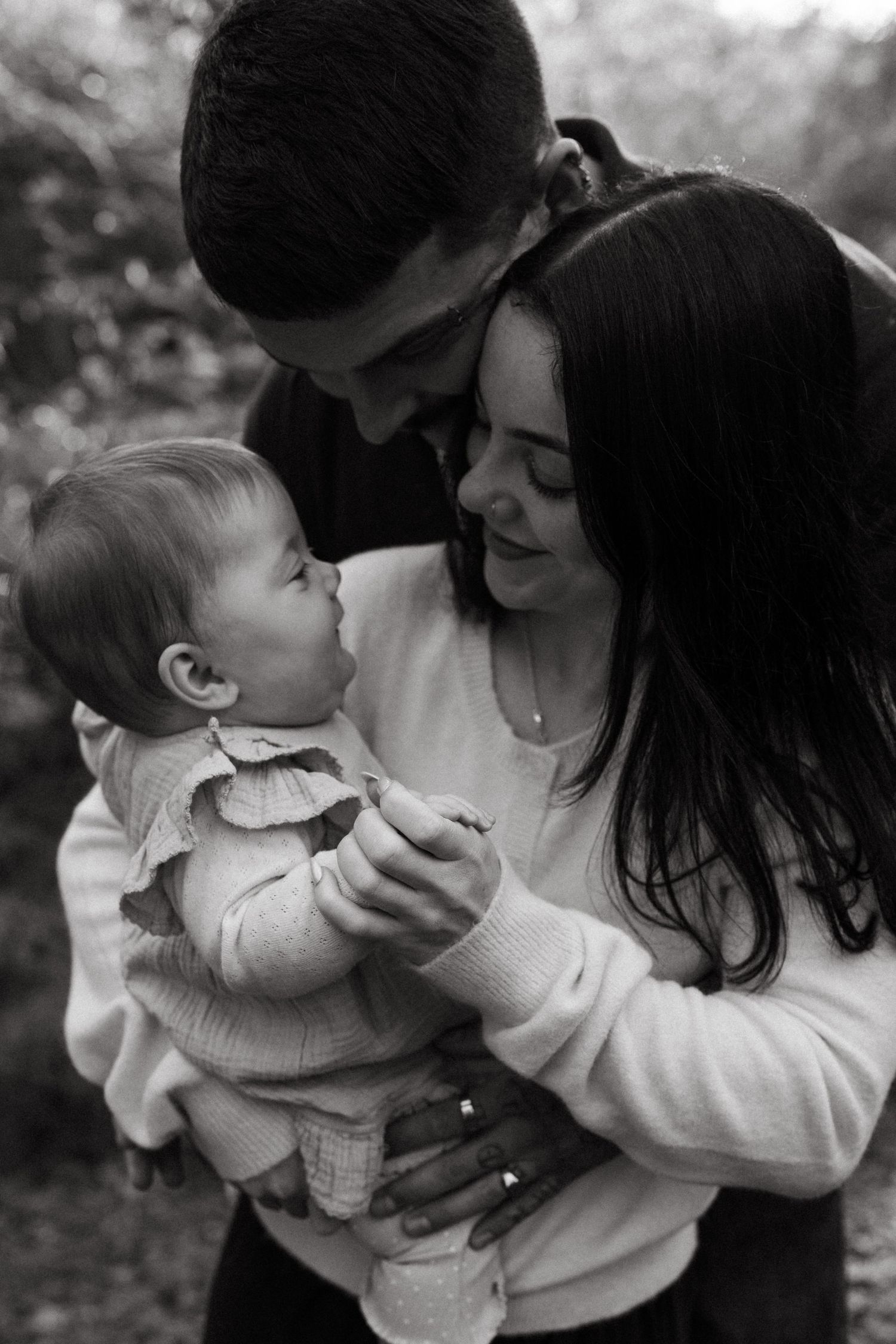 Black and white photo of parents lovingly gazing at their baby girl outdoors.