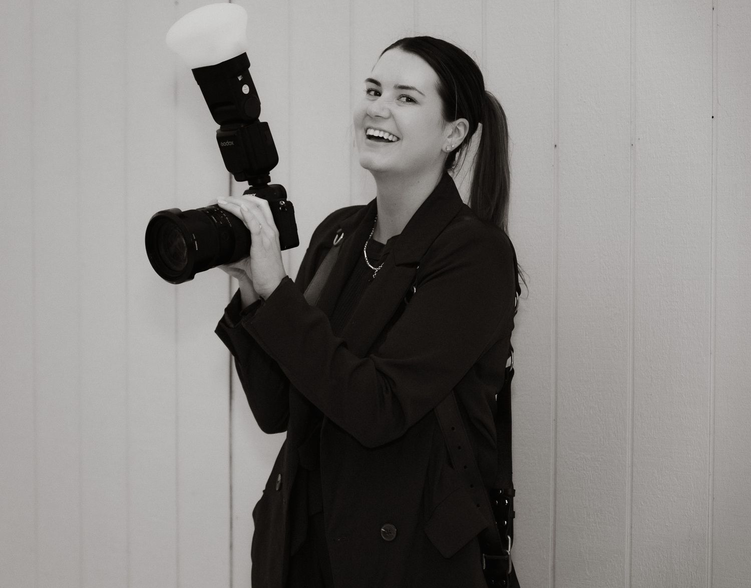 Black and white photo of a Katie Charlotte holding a professional camera with flash attachment.