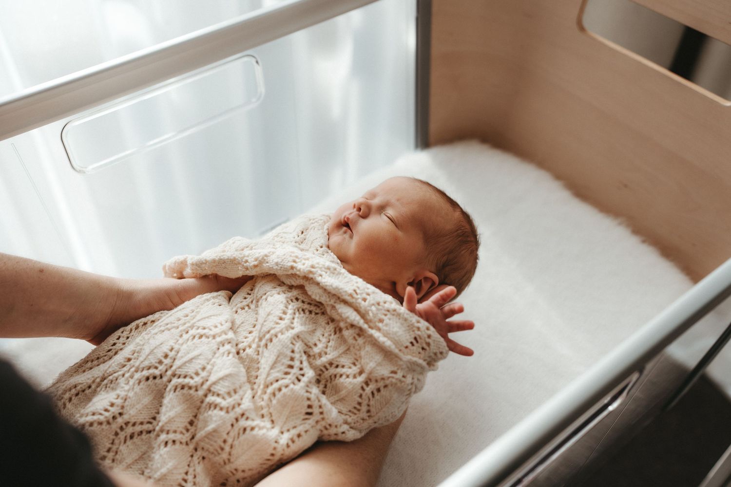Peaceful newborn baby swaddled in a knit blanket resting in a bassinet.