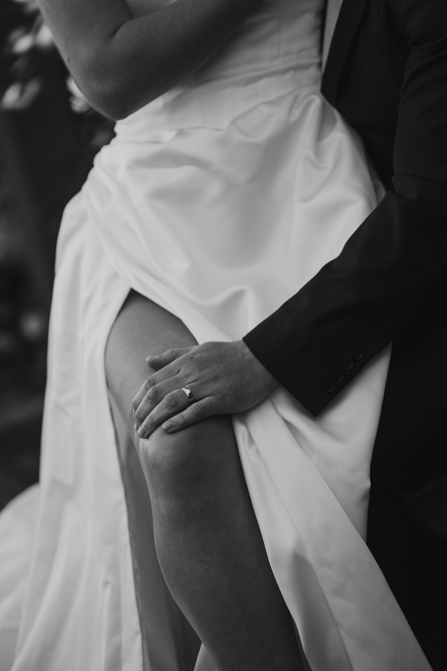 Black and white close-up of groom embracing bride in white wedding dress showing diamond ring.