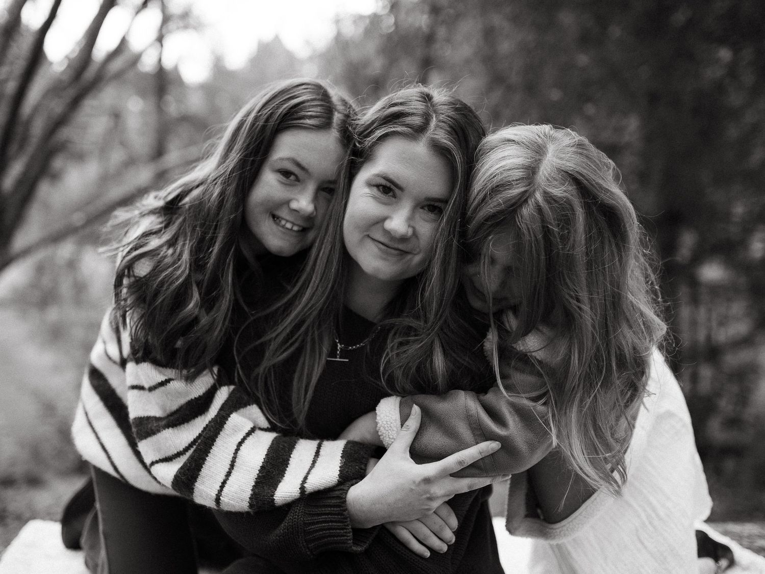 Three young women smiling and hugging each other outdoors in a black and white portrait photo.