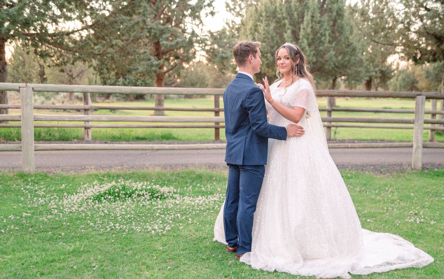 Wedding couple posing on grass lawn with rustic wooden fence.