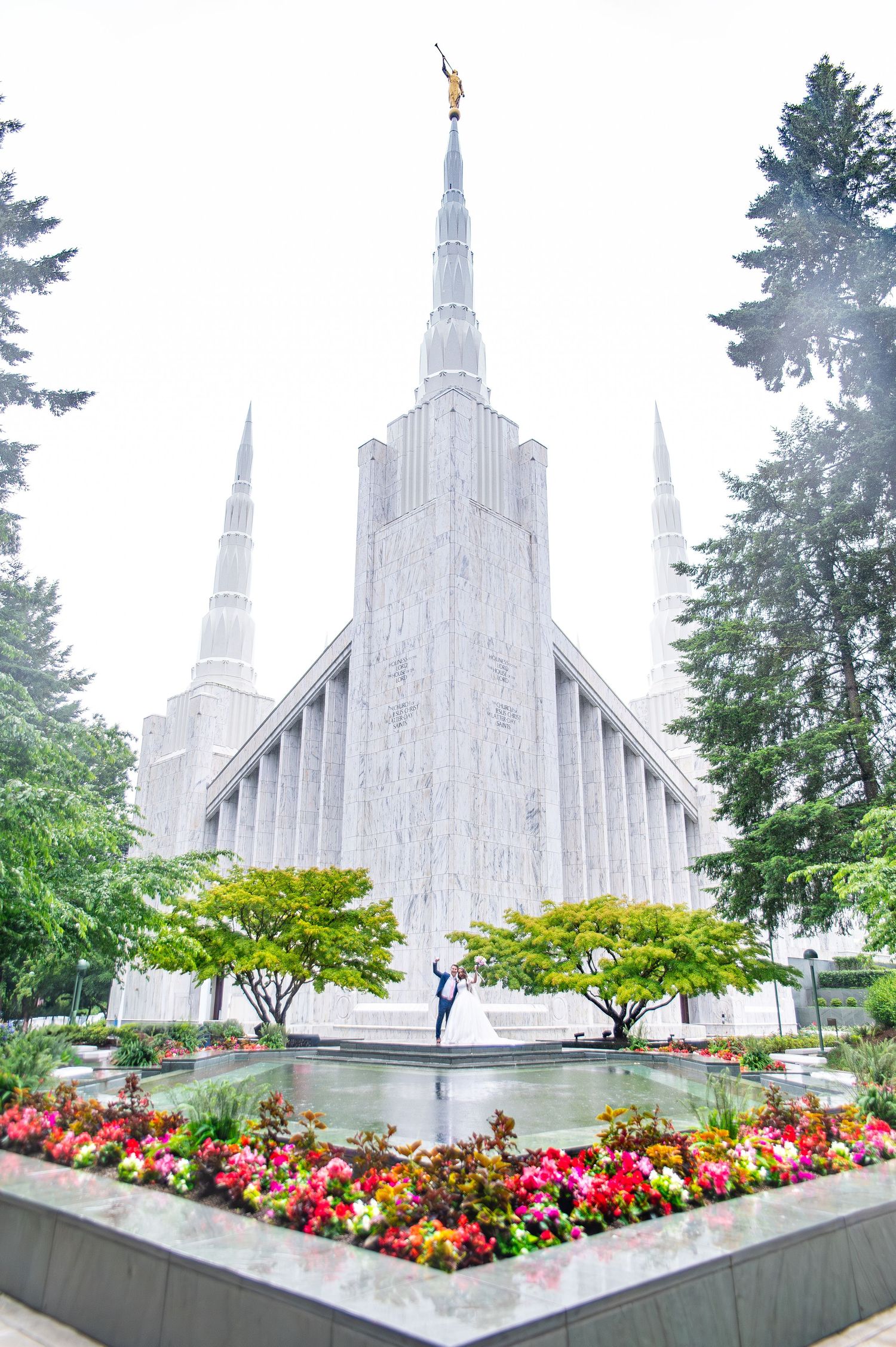 Mormon temple exterior with vibrant flower gardens and white architecture against cloudy sky.