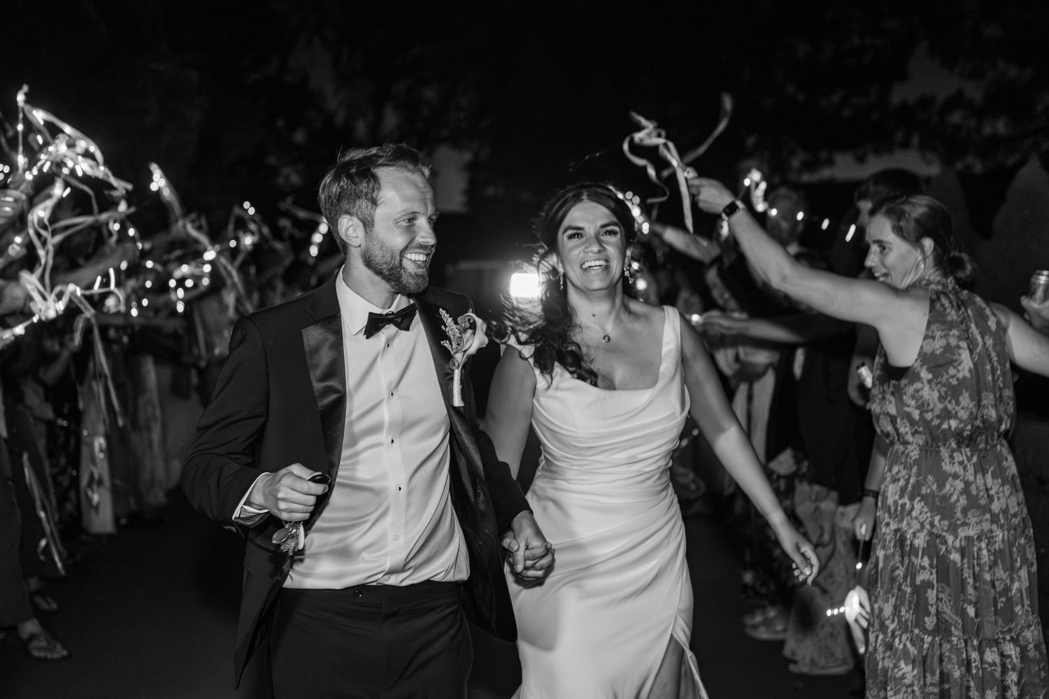 Black and white photo of a bride and groom walking through a sparkler exit at their wedding reception.