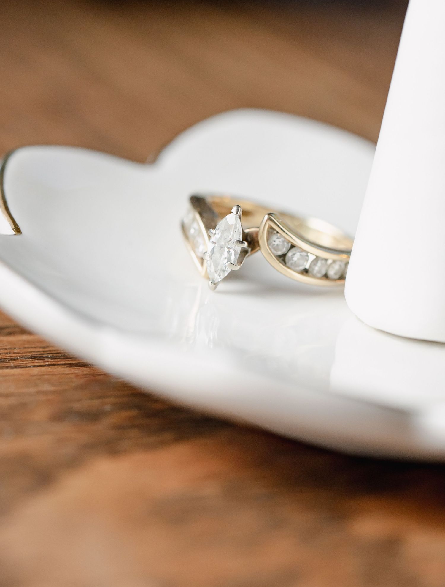 Diamond engagement ring displayed on white ceramic surface with wooden background.