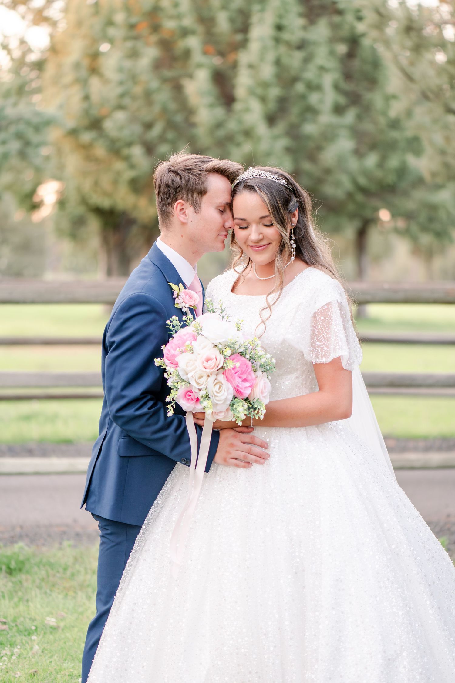 Wedding portrait showcasing flowing white gown and pink floral bouquet in natural setting.